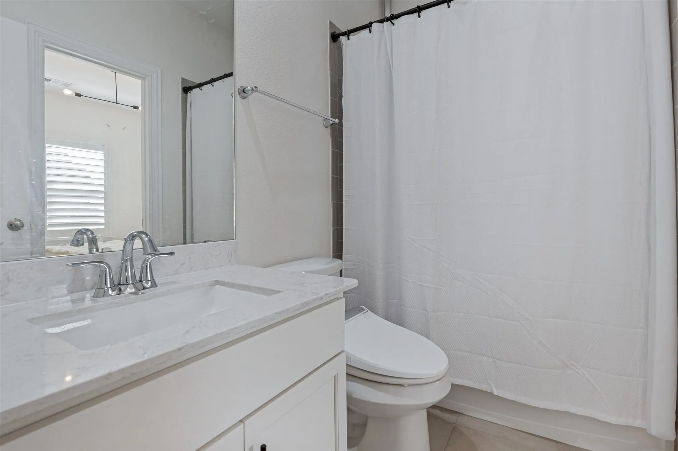 Bathroom featuring a vanity with a white countertop and undermount sink, chrome faucet, white cabinetry, and a shower with tile surround