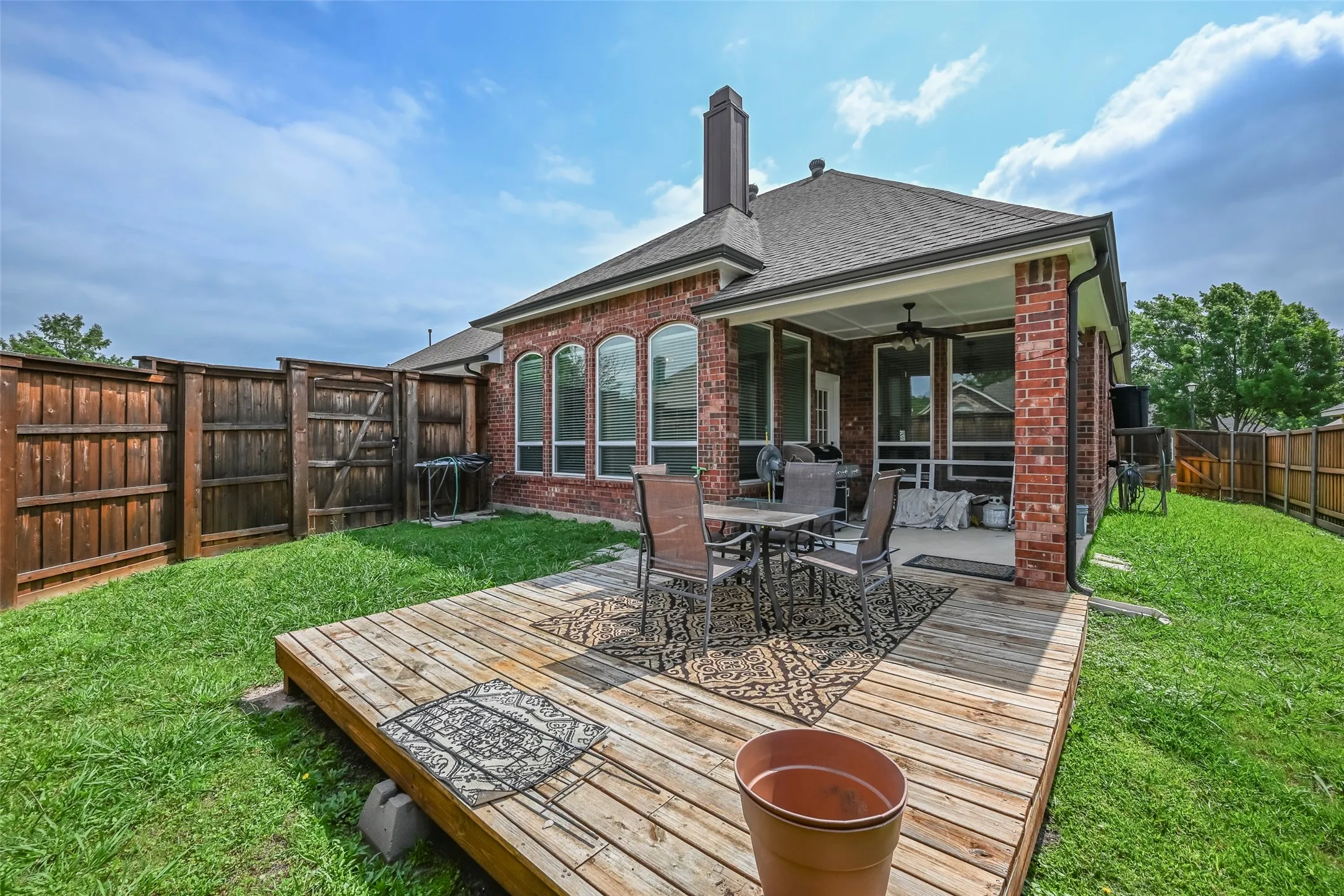 Spacious backyard featuring a substantial wood deck, an attached covered patio with a ceiling fan, and a privacy fence