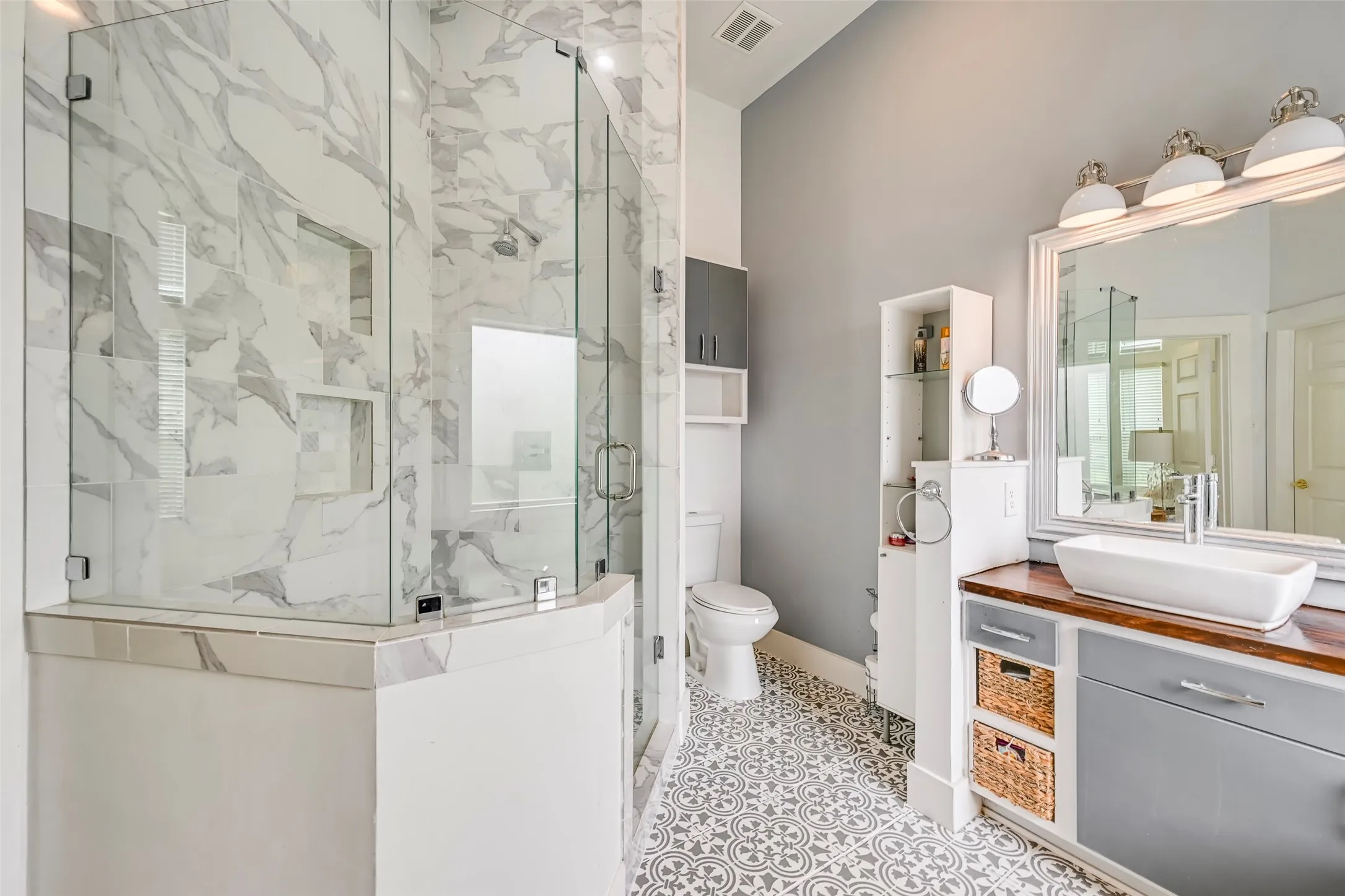 Glass-enclosed shower with full-height marble-look tile surround and integrated shelving