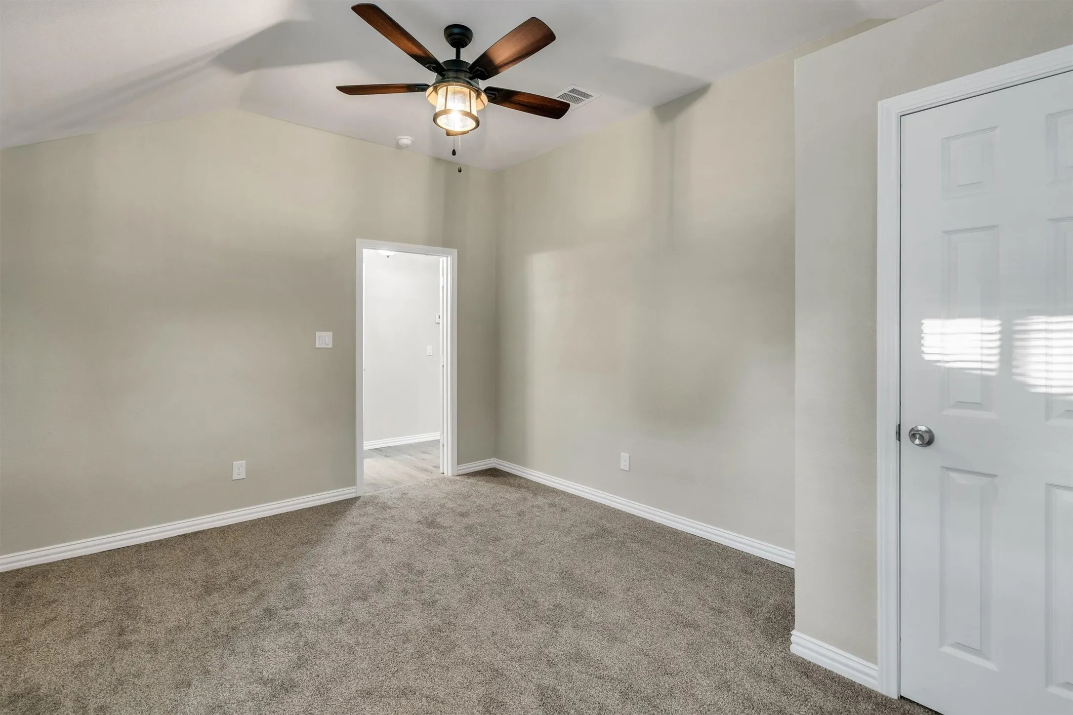 Interior room featuring vaulted ceilings, a ceiling fan with integrated lighting, neutral wall tones, plush gray carpeting, and white trim