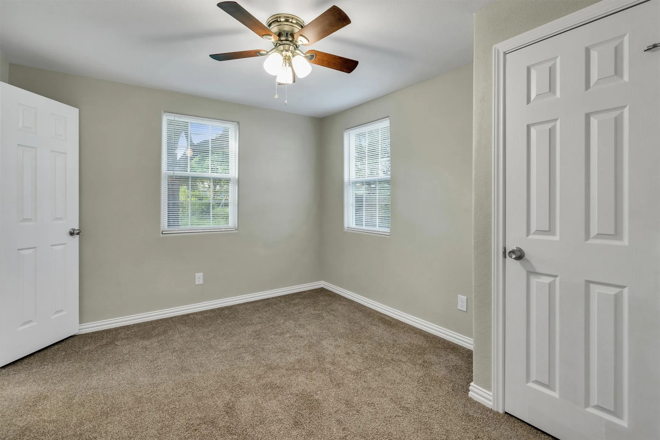 Carpeted interior room featuring a ceiling fan with light fixture, two windows, and white trim molding