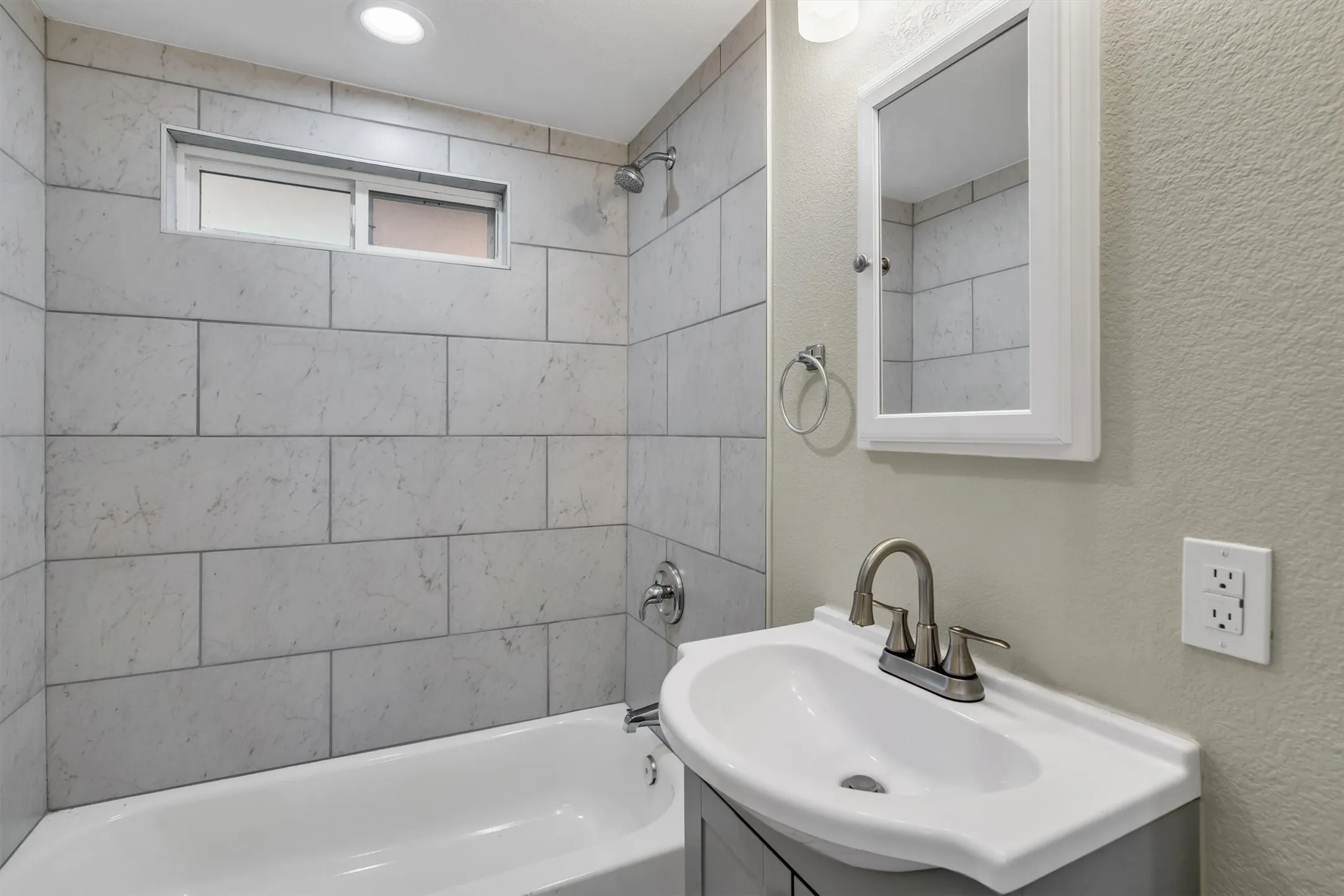 Full bathroom featuring a white bathtub, light-toned wall tile, a recessed window, and a vanity with a white sink and brushed nickel faucet