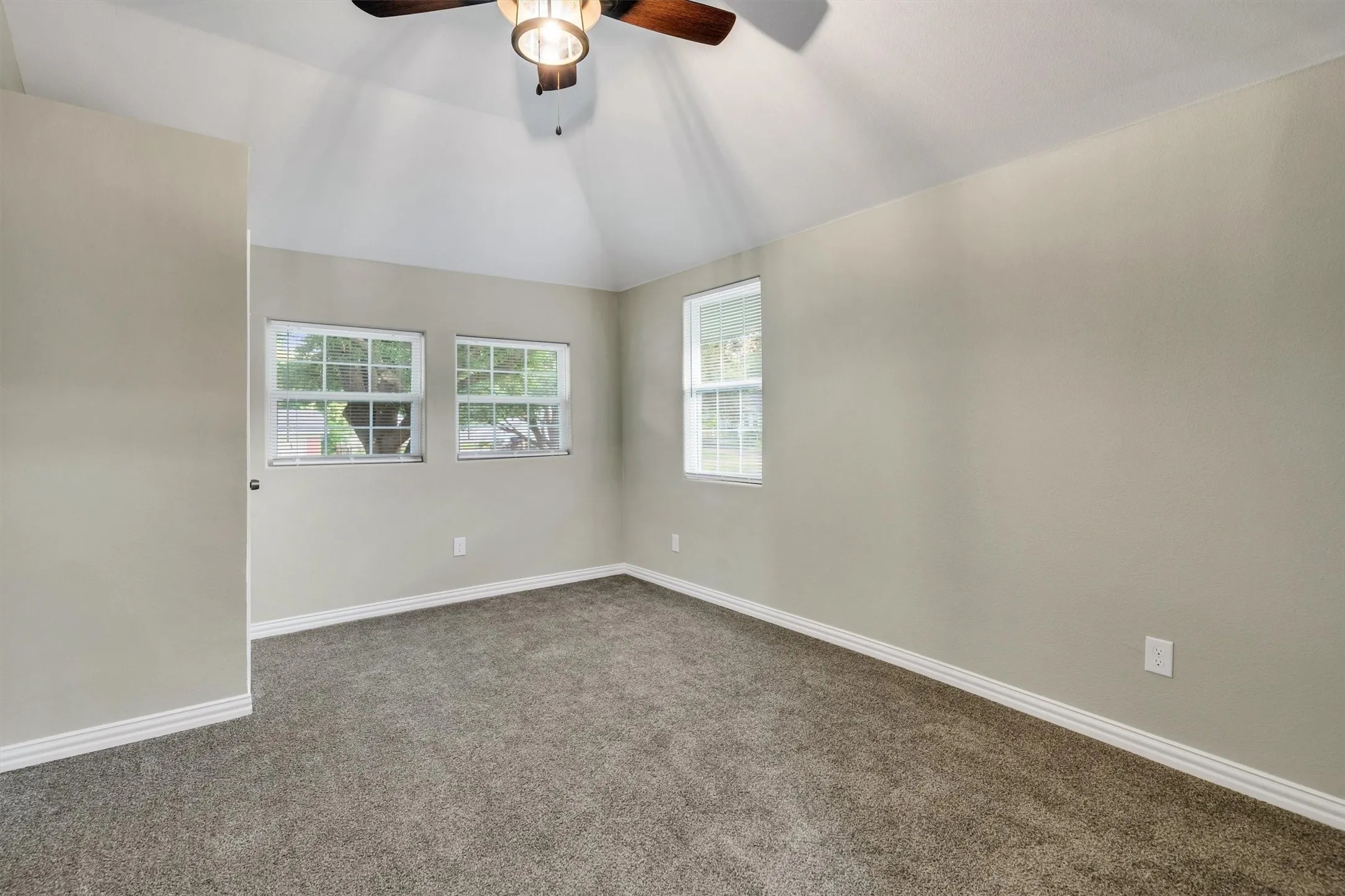 Vaulted ceiling bedroom featuring carpeting, multiple windows, and a ceiling fan with integrated lighting