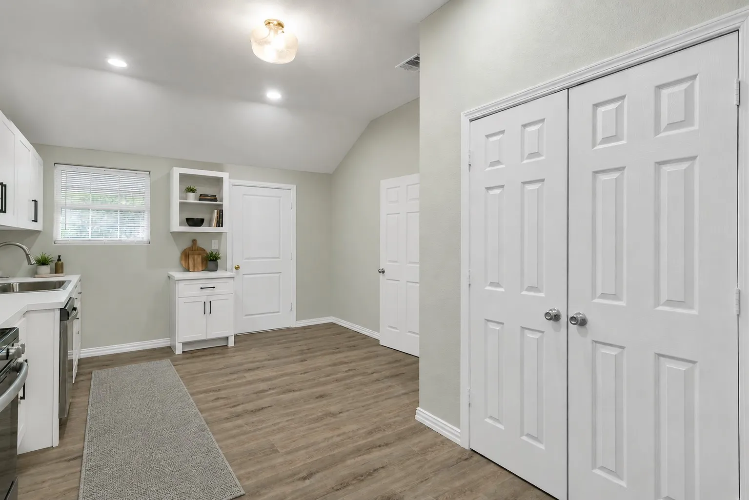 Kitchen area featuring wood-finish flooring, white cabinetry, a stainless steel sink, and light-colored countertops