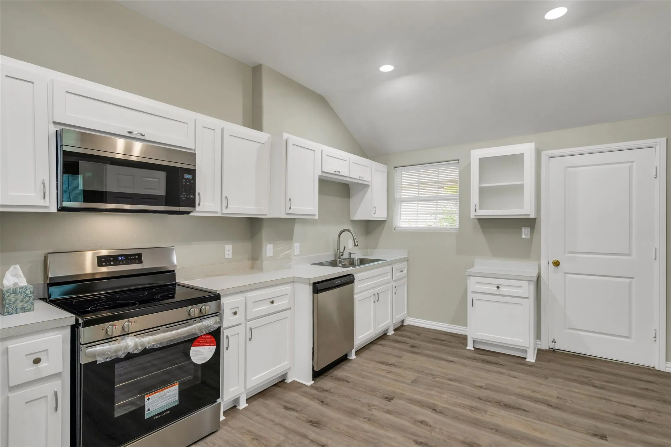 Modern kitchen featuring white shaker cabinetry, stainless steel appliances, light countertops, wood-finish flooring, and recessed lighting
