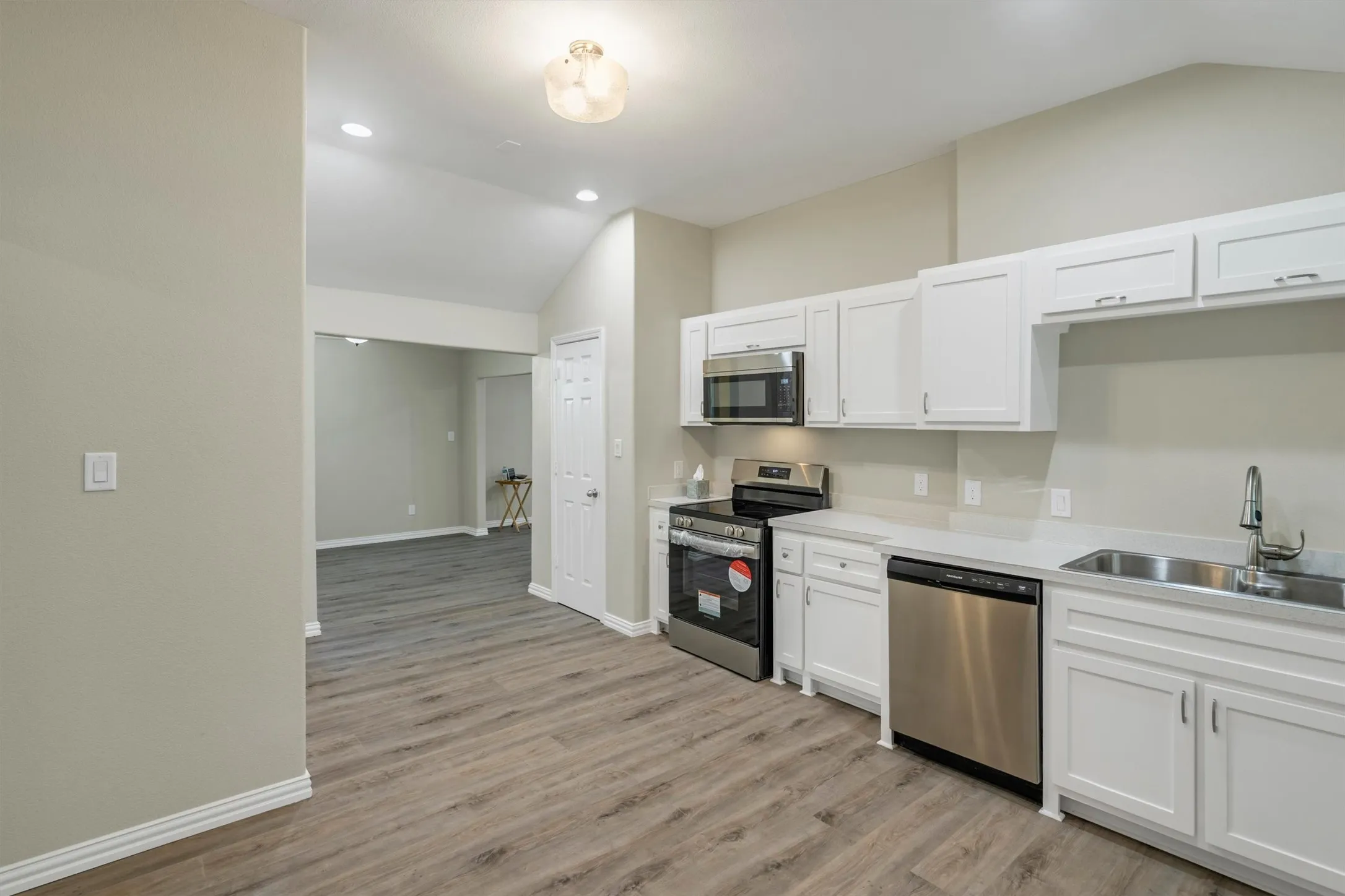 Kitchen featuring white cabinetry, stainless steel appliances, light countertops, and wood-finish flooring