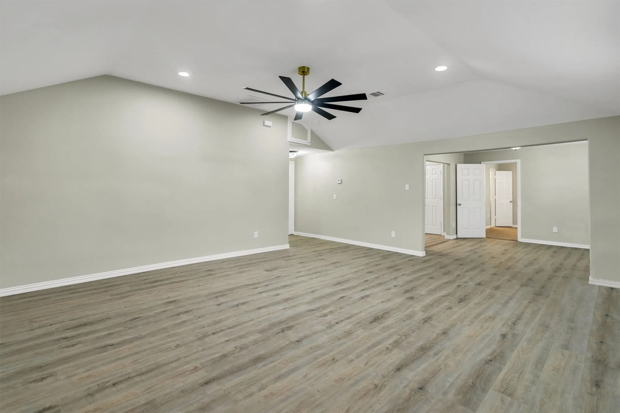 Spacious room featuring vaulted ceilings, recessed lighting, a modern ceiling fan with black blades, and light-toned wood-finish flooring