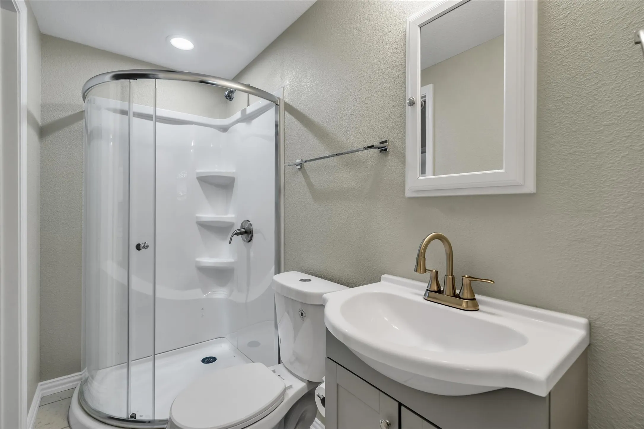 Compact bathroom featuring a curved glass shower enclosure, a single vanity with an integrated sink, a bronze-finish faucet, and a wall-mounted medicine cabinet