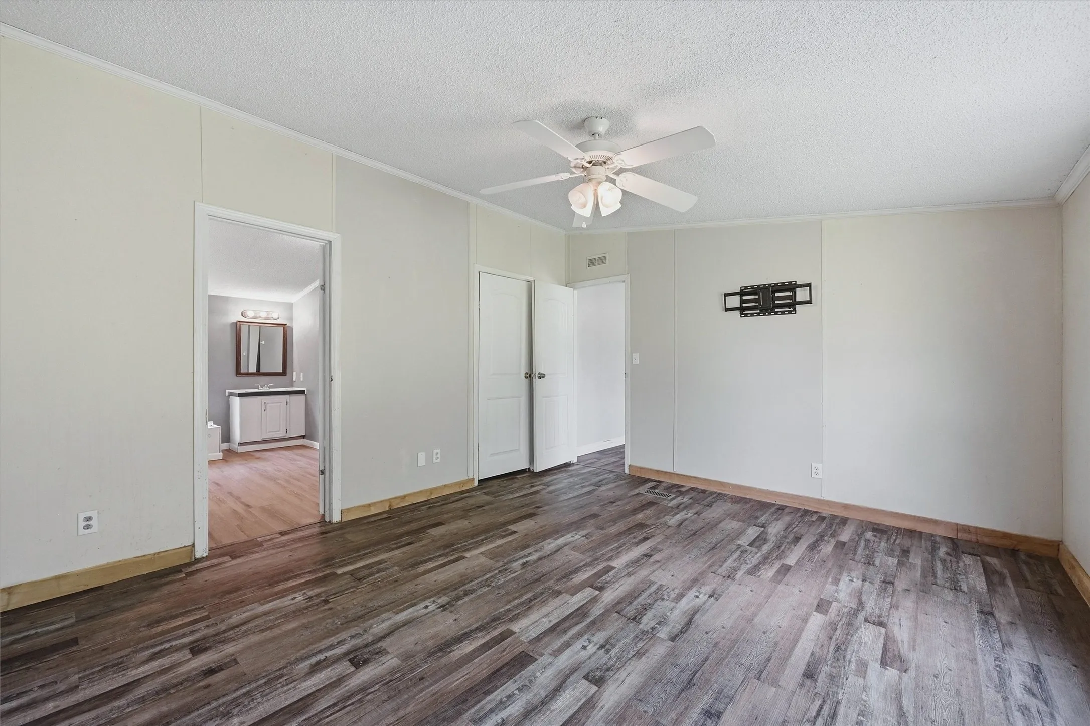 Spacious interior room featuring wood-finish flooring, light-toned wall paneling, and a ceiling fan
