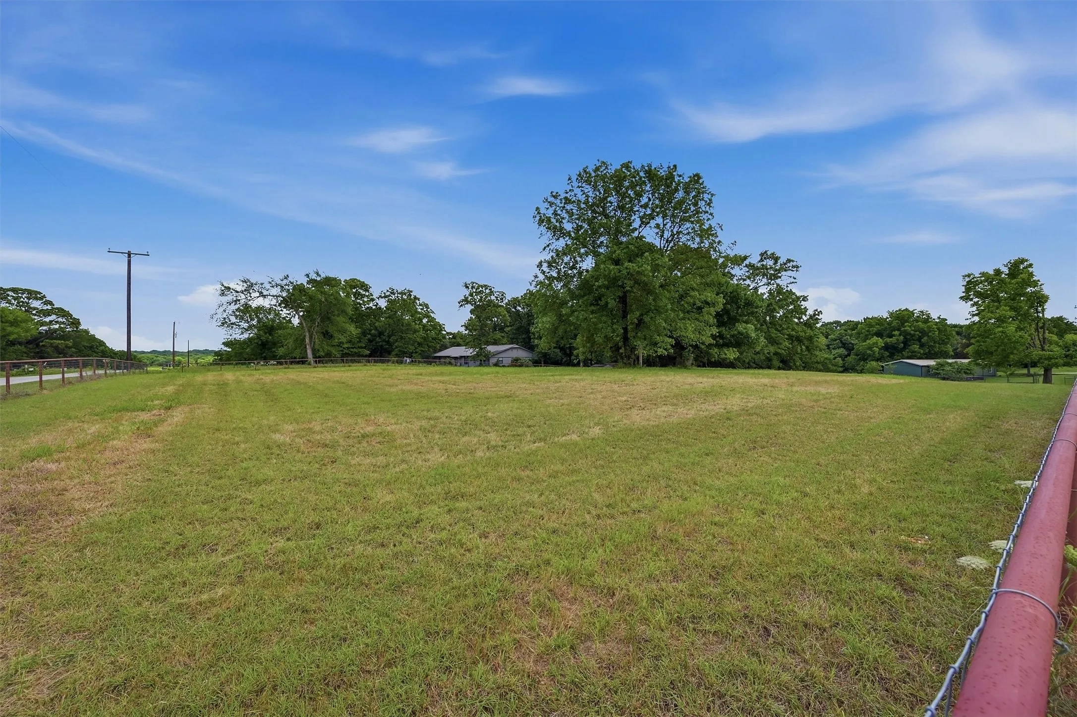 Expansive green field with natural tree lines and blue sky