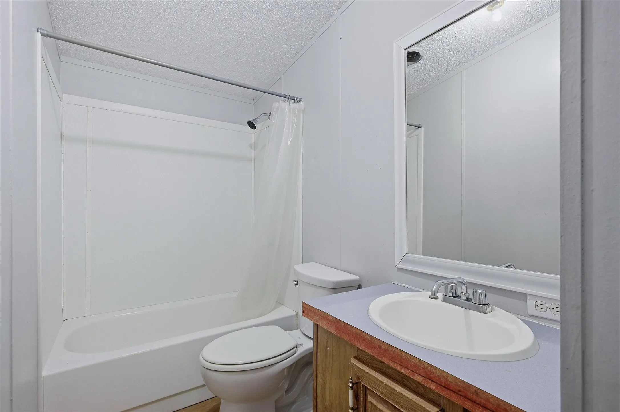 Bathroom featuring a white tub-shower combination, a vanity with a drop-in sink, a wall-mounted mirror, and a ceiling light fixture