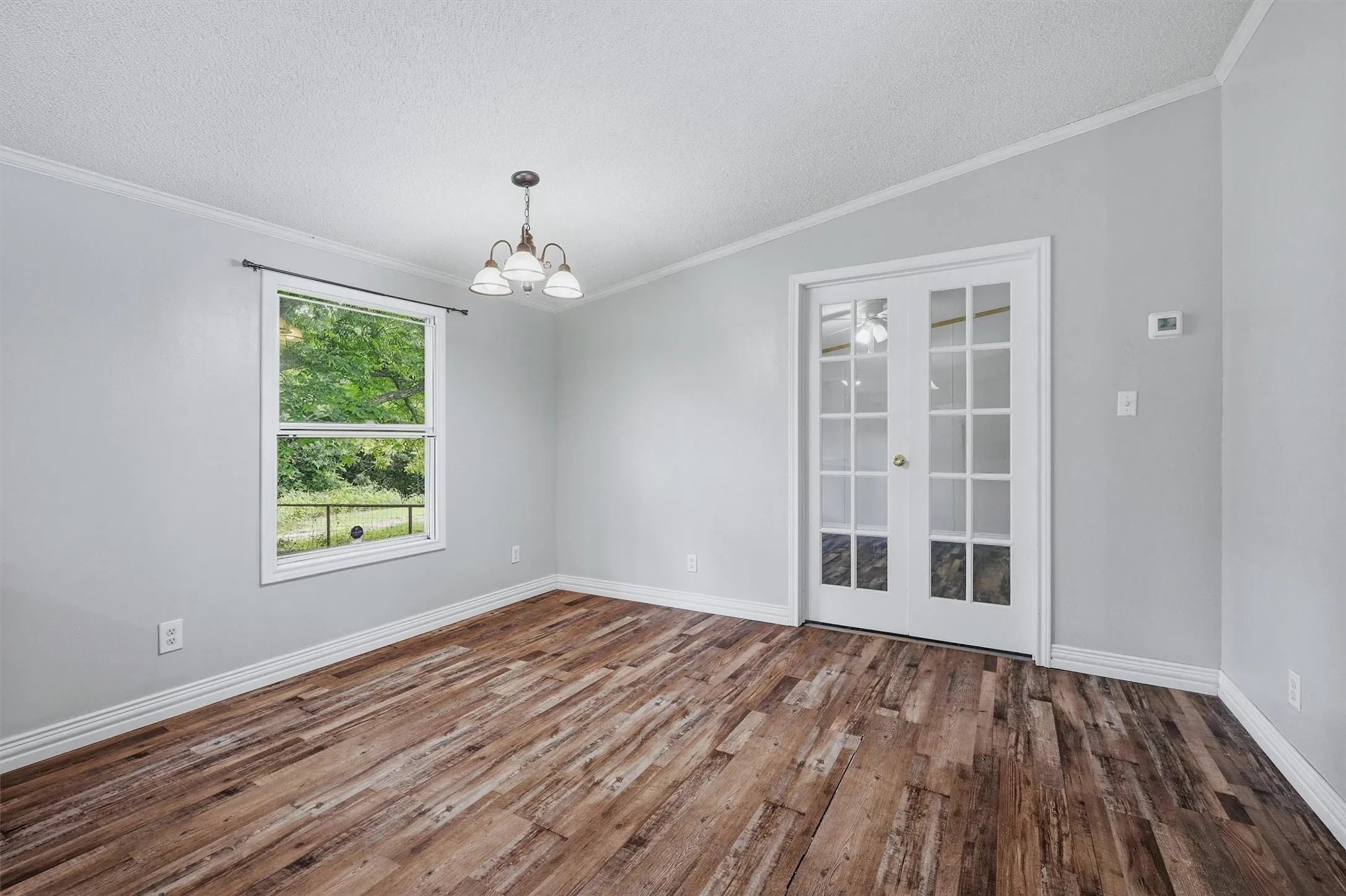 Vaulted ceiling room featuring wood-finish flooring, white baseboards, and a contemporary chandelier
