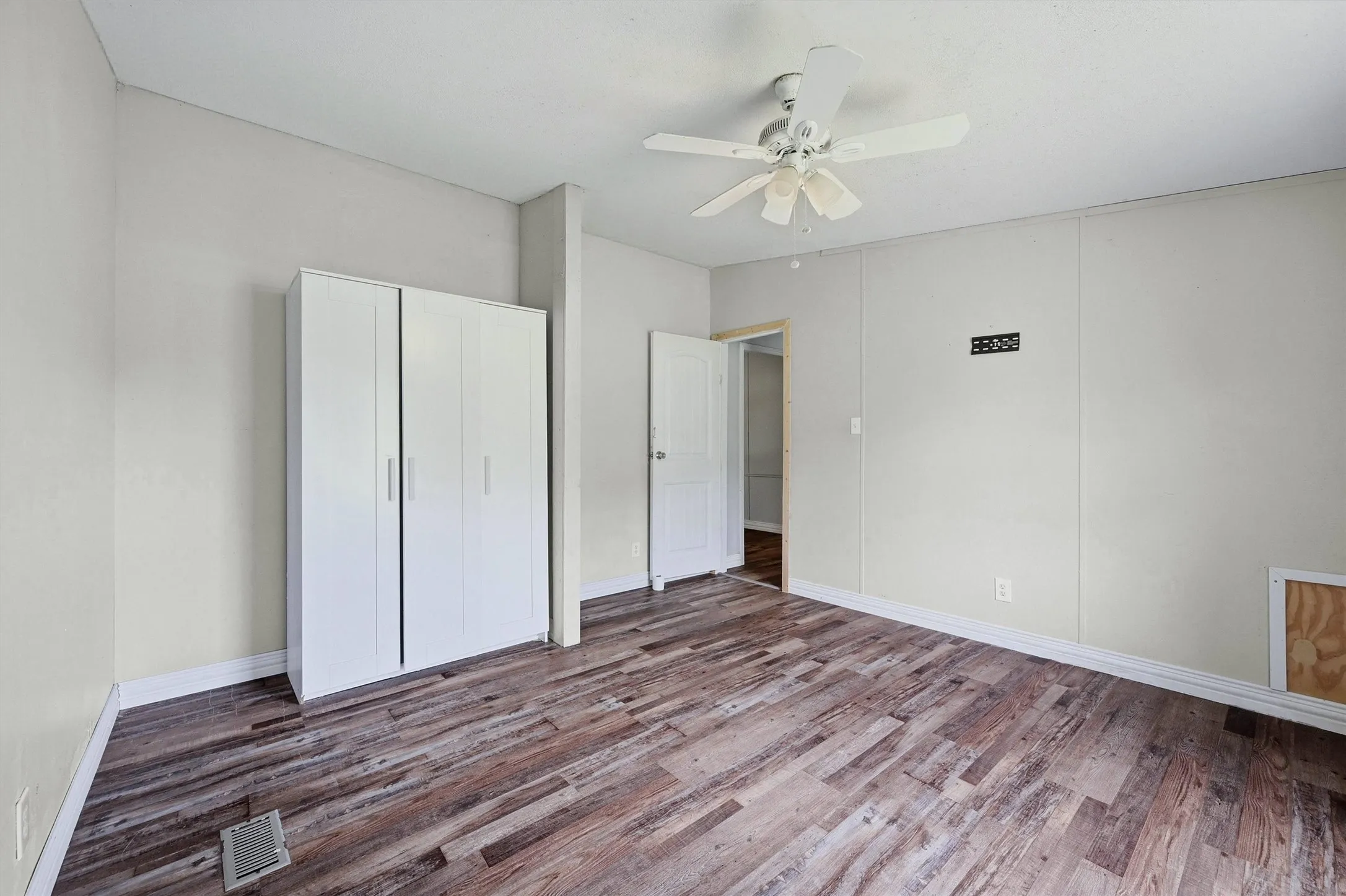 Room featuring wood-finish flooring, light-toned wall paneling, and a white ceiling fan
