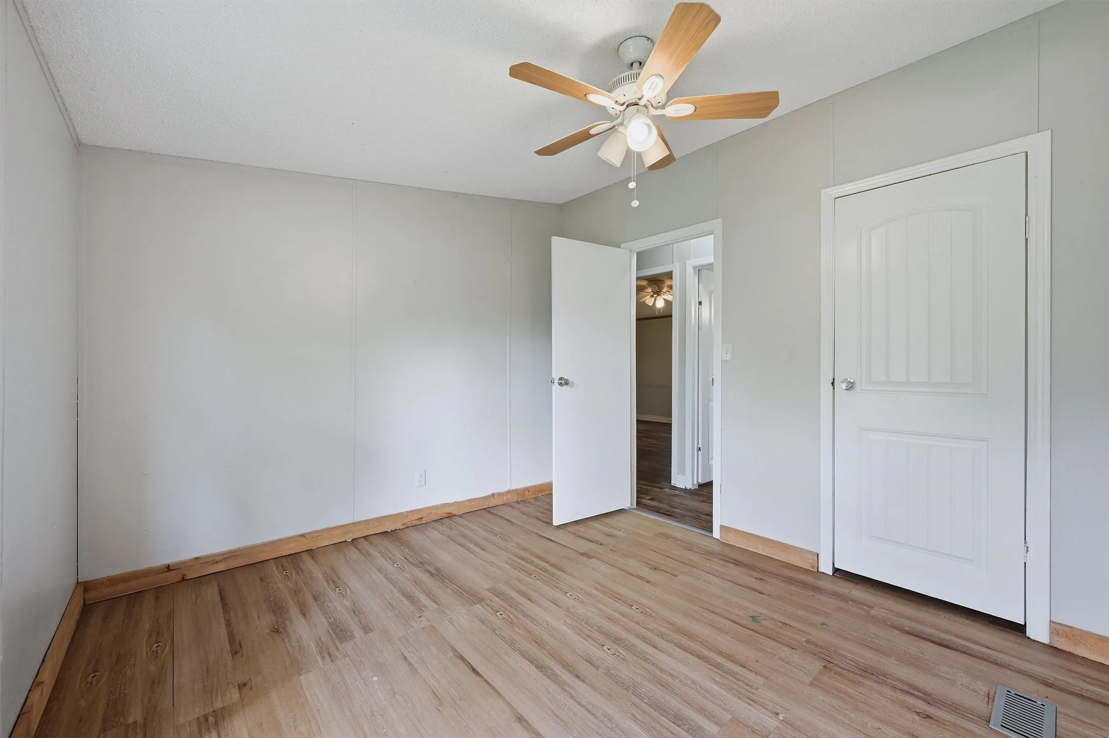 Room featuring wood-finish flooring, a ceiling fan with light fixture, and light gray wall paneling