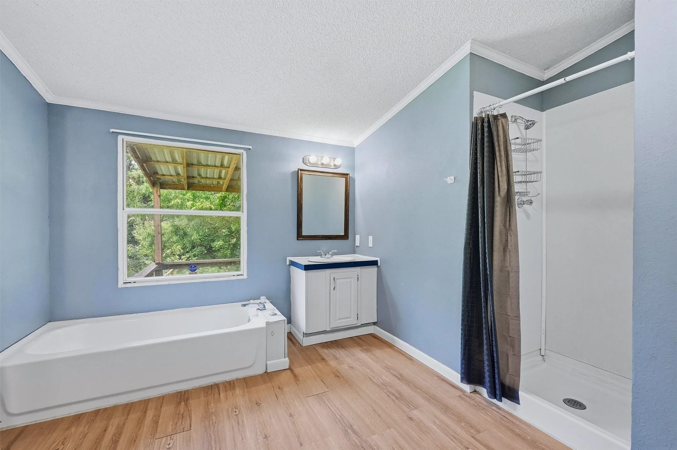 Bathroom featuring a single window, a built-in tub, wood-finish flooring, a vanity with a white countertop, and a stand-up shower