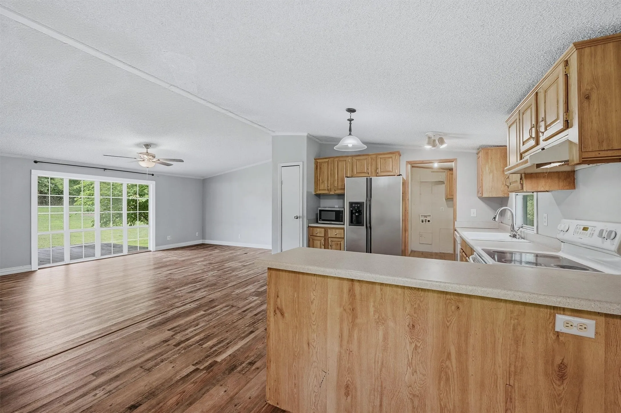 Spacious open-concept living area featuring wood-finish flooring, a ceiling fan with integrated lighting, and white trim throughout
