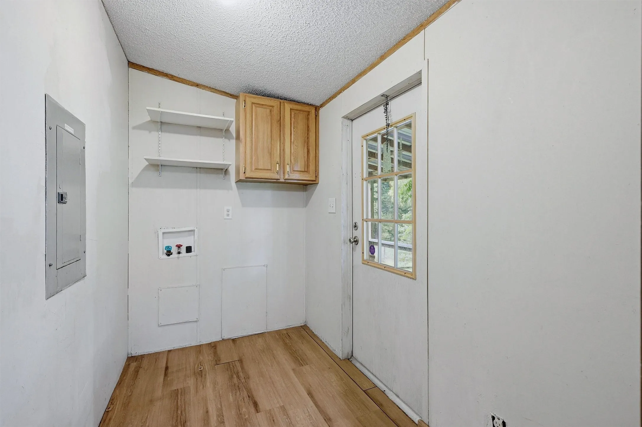 Utility room featuring wood-finish flooring, wall-mounted shelving, built-in cabinetry, and an exterior door with a window pane