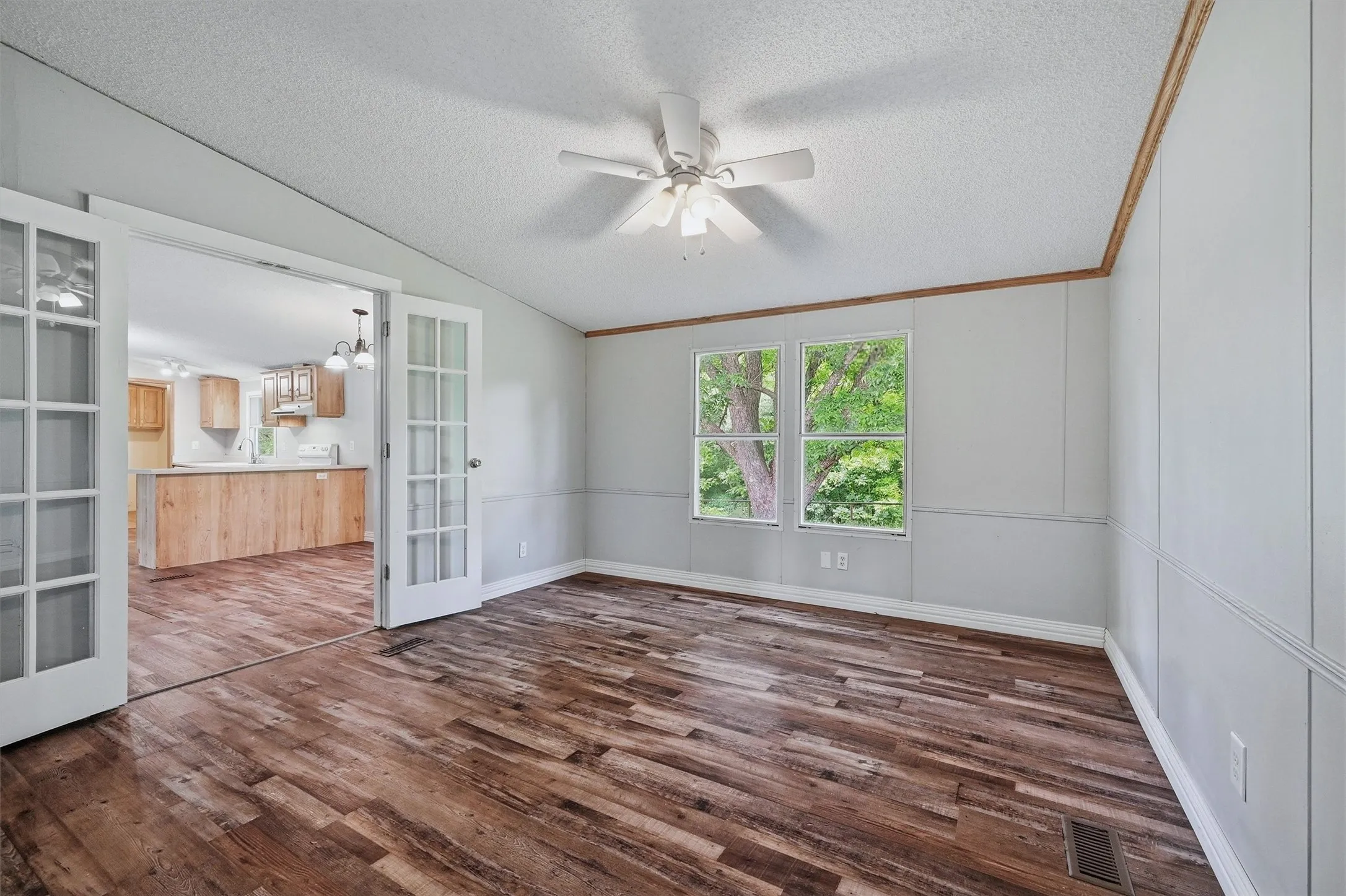 Room featuring wood-finish flooring, white paneled walls, and two windows with exterior views