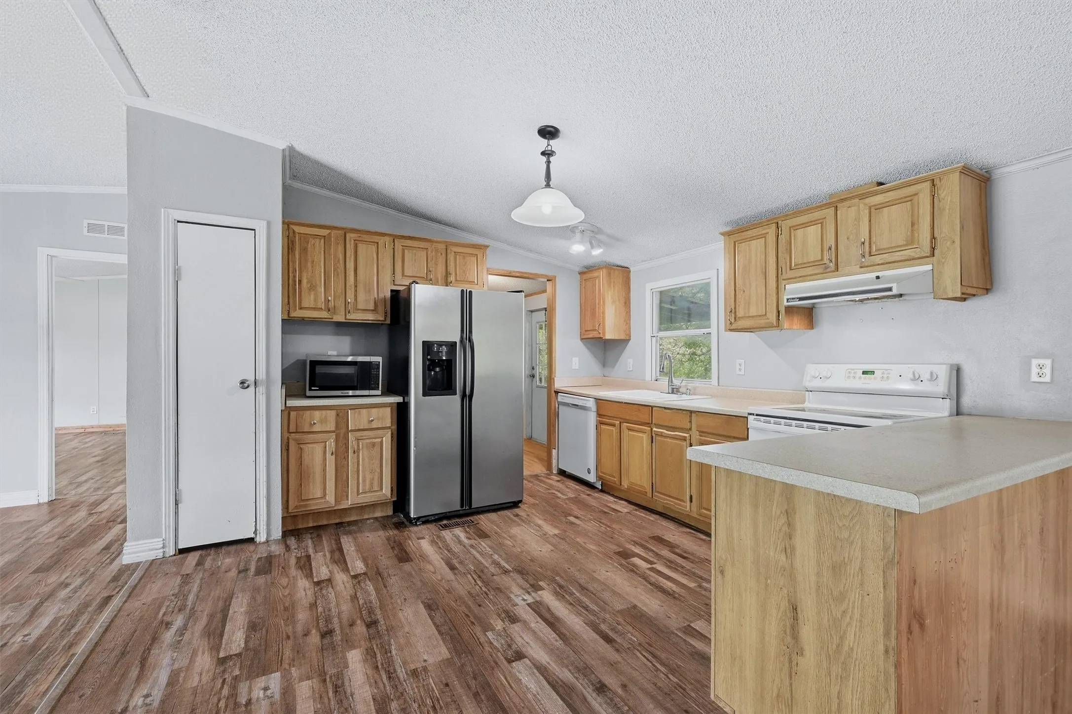 Kitchen featuring wood-finish flooring, light wood cabinetry, stainless steel refrigerator, white range, and a built-in kitchen island with countertop space