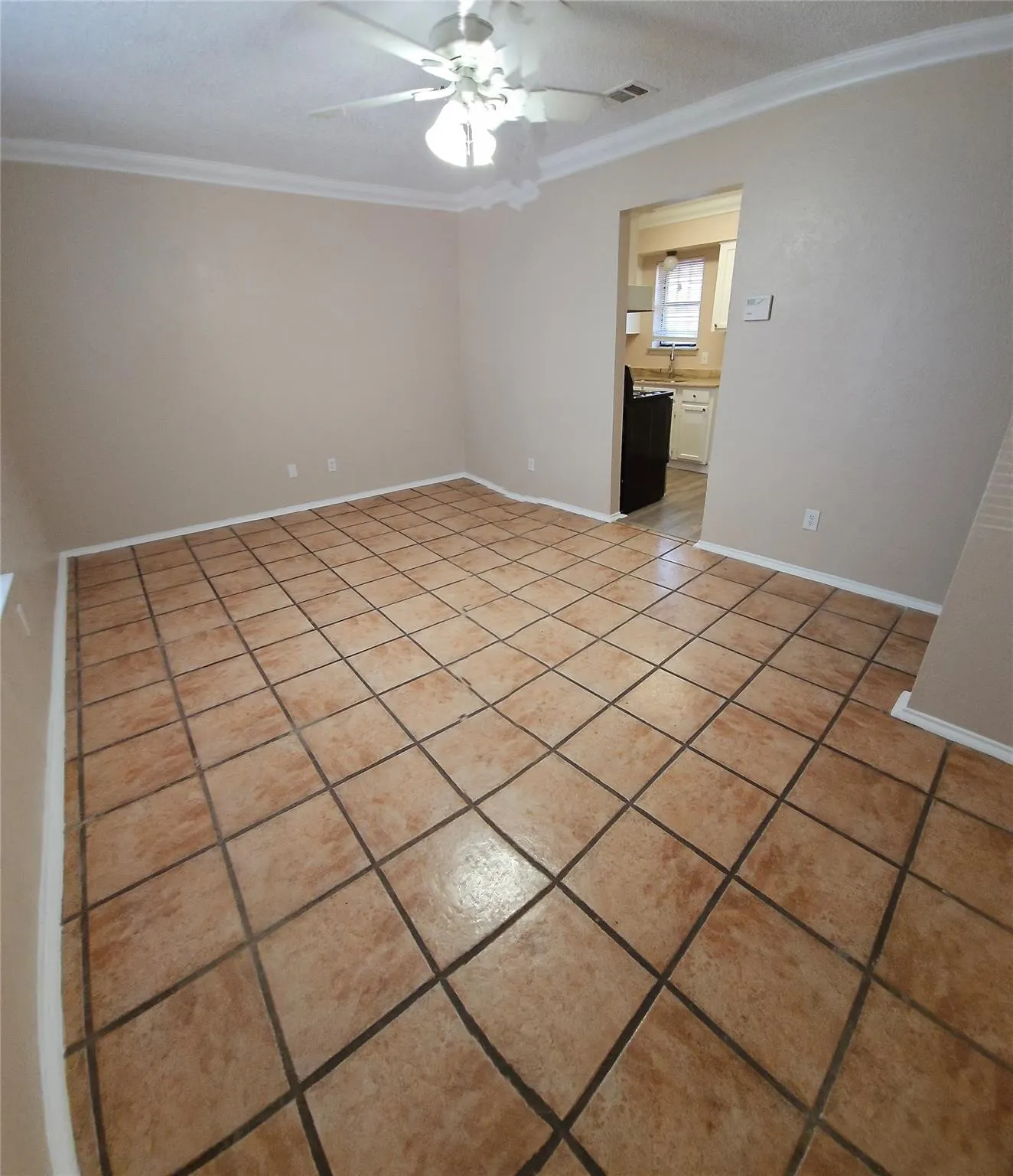 Spacious room featuring tile flooring, neutral wall tones, crown molding, and a ceiling fan with integrated lighting