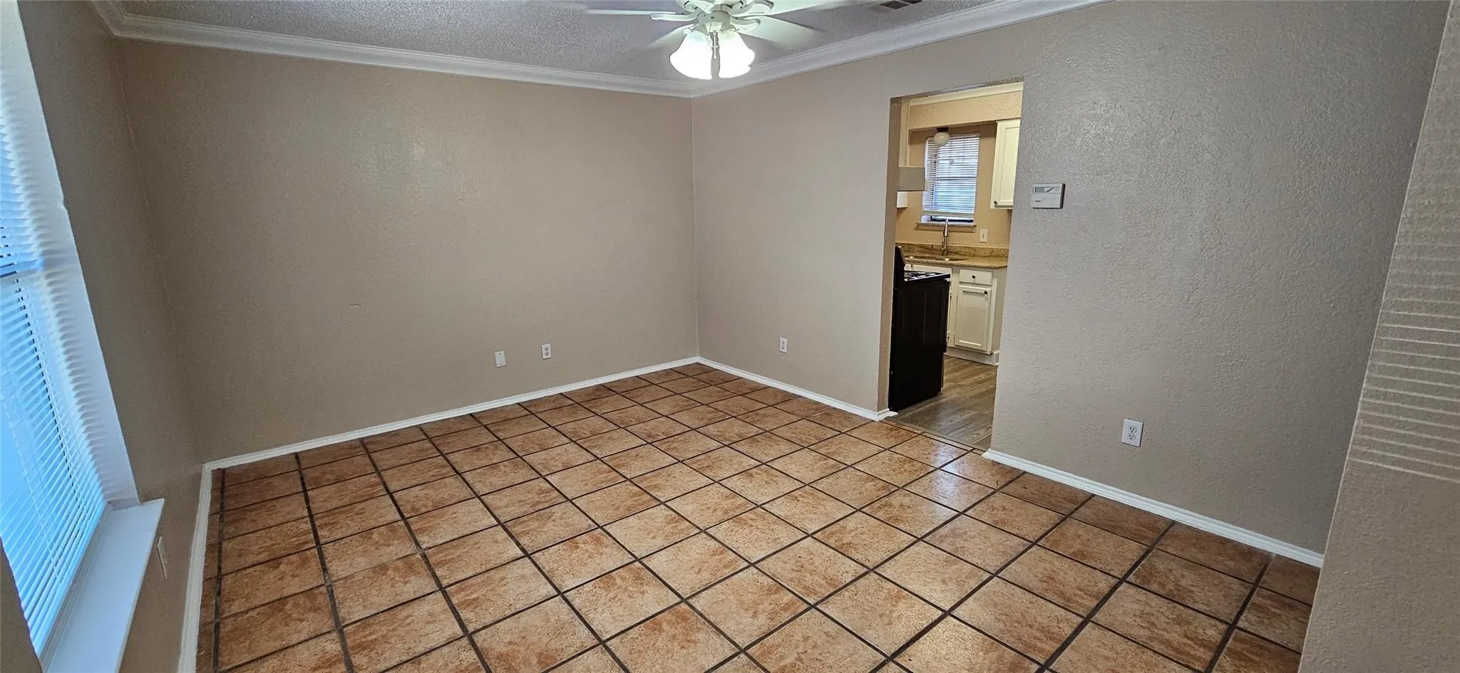 Spacious room featuring large format ceramic tile flooring, crown molding, and a ceiling fan with integrated lighting