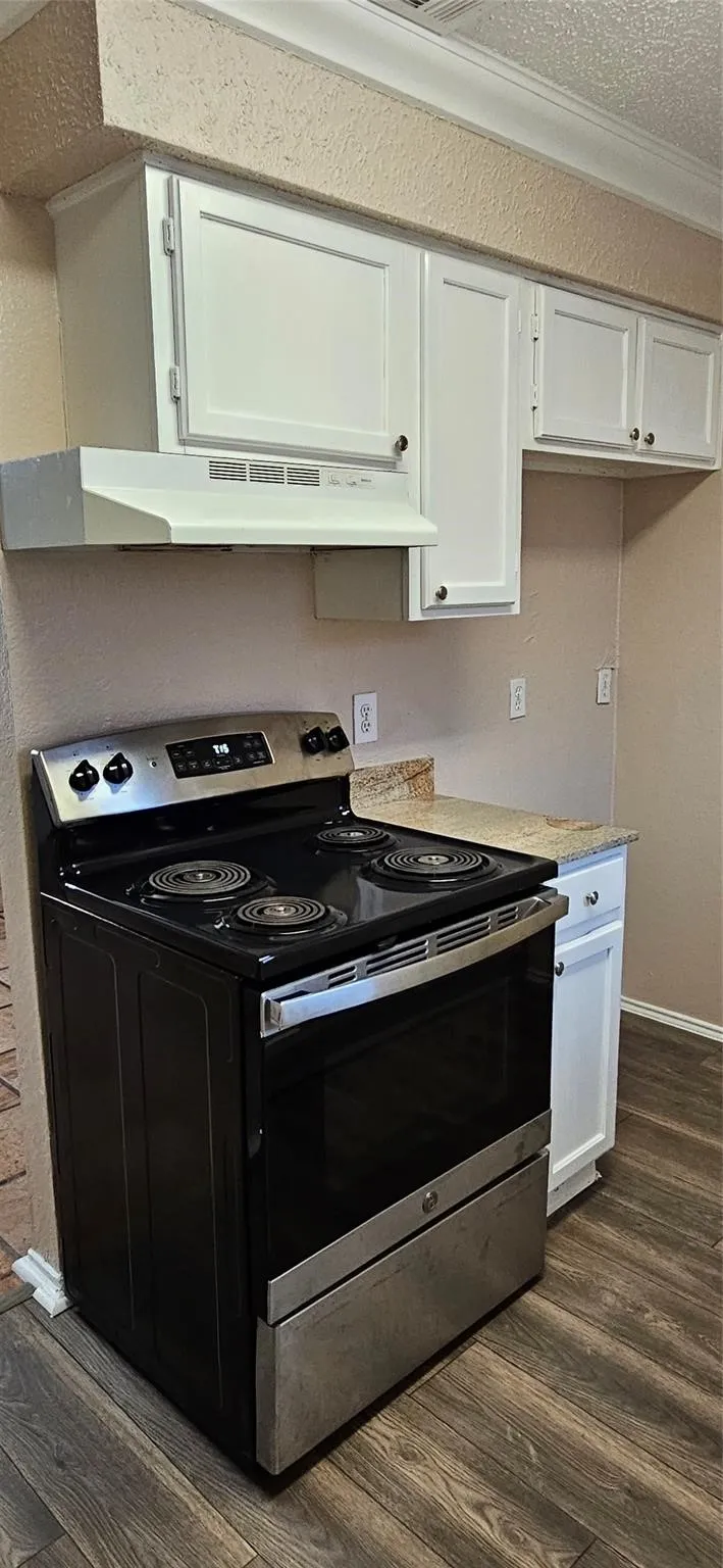 Kitchen area featuring a black and stainless steel range with overhead ventilation, white cabinetry, and wood-finish flooring