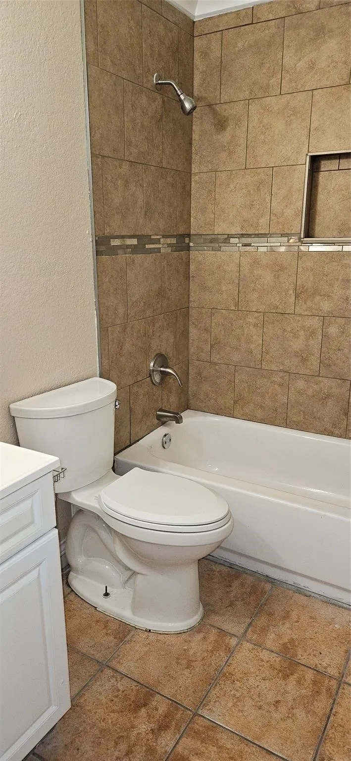 Bathroom featuring a tiled shower surround with a decorative accent band and recessed niche, a white tub, a white toilet, and tile flooring