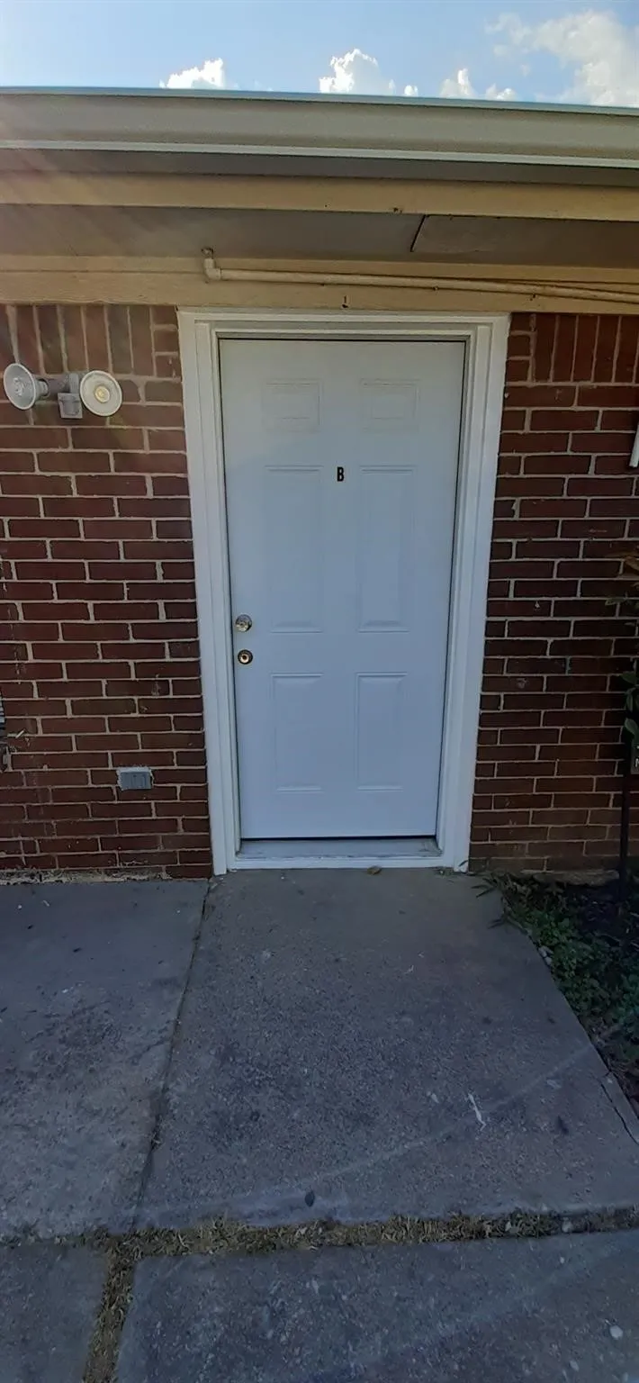 White four-panel entry door with a door viewer, set against a red brick exterior