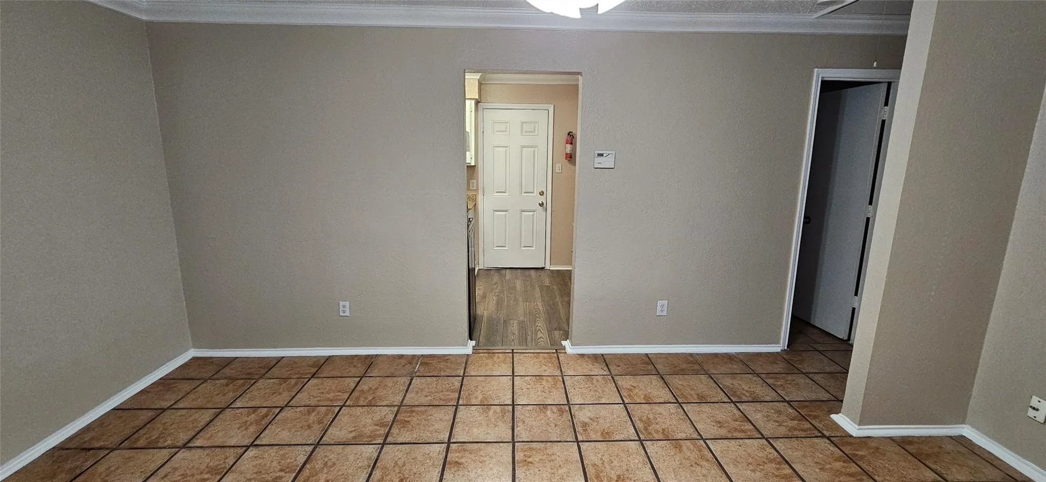 Spacious room featuring neutral tone walls, crown molding, and large format tiled flooring