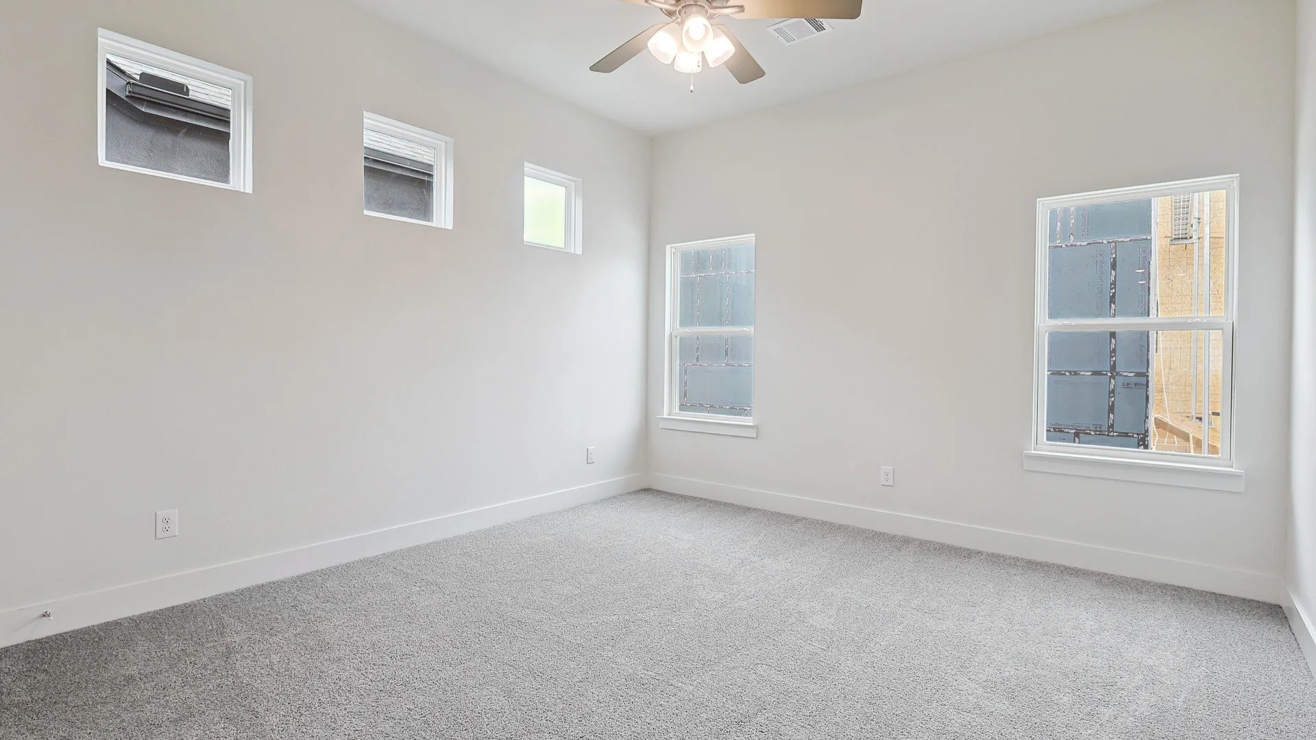 Spacious room featuring light gray carpeting, multiple windows, high ceilings, and a ceiling fan with integrated lighting
