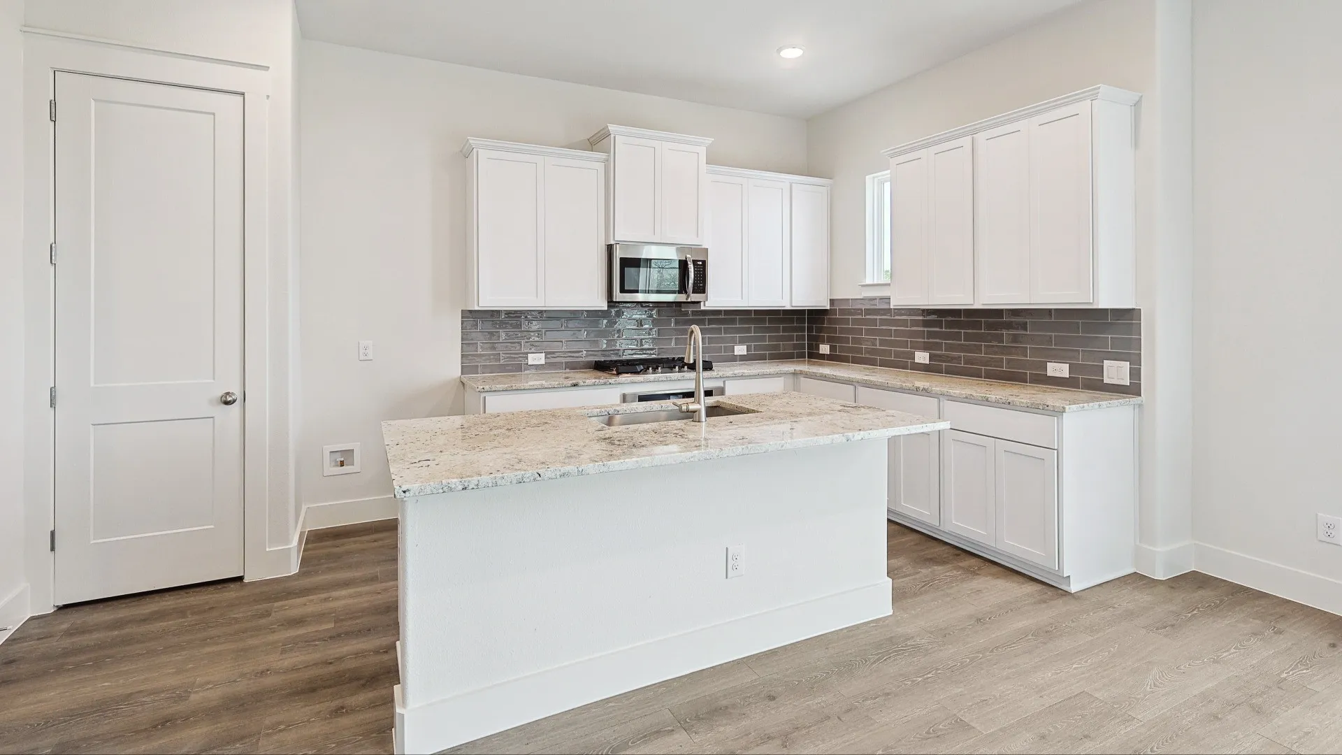 Kitchen featuring an island with a breakfast bar extension, white cabinetry, integrated stainless steel microwave, and gray subway tile backsplash