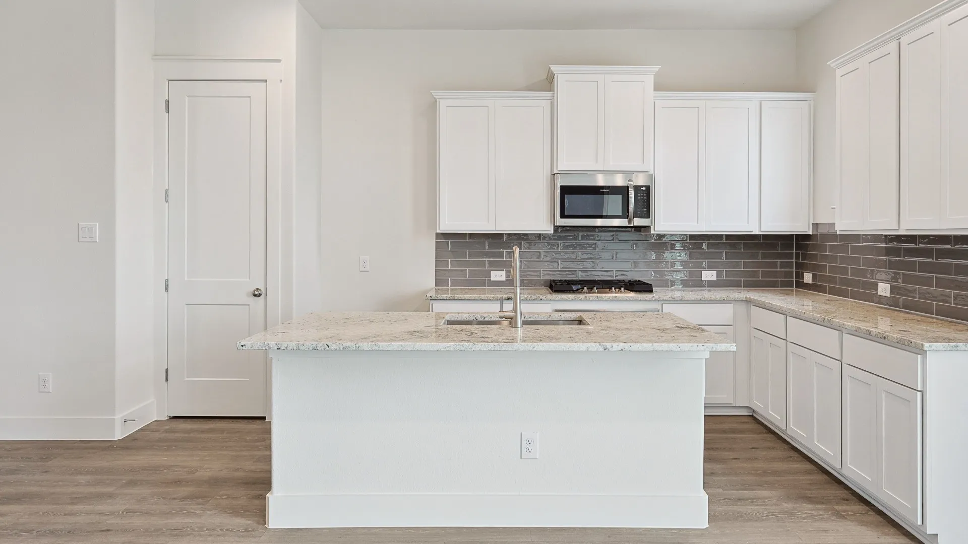 Kitchen featuring a large island with an integrated sink, white cabinetry, speckled countertops, stainless steel appliances, and a gray subway tile backsplash