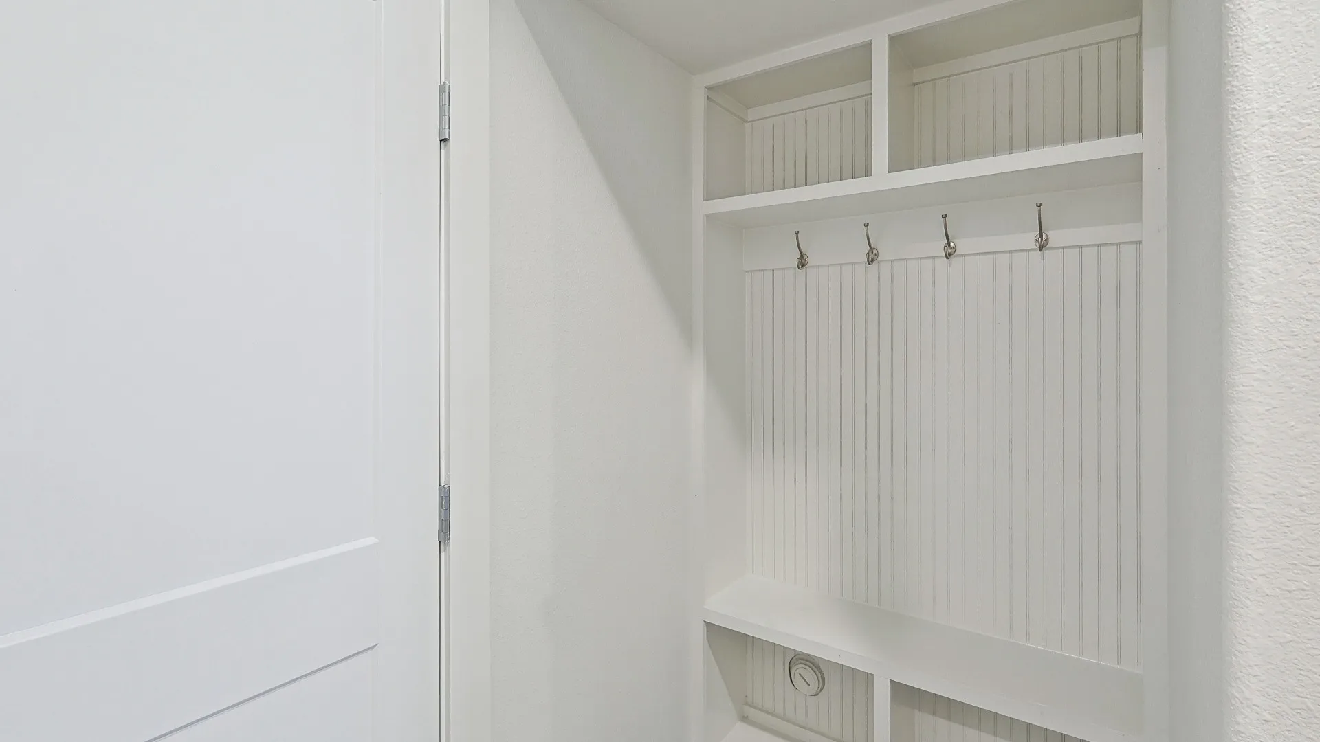 Built-in mudroom station featuring beadboard backing, four metal hooks, open shelving, and lower cubbies