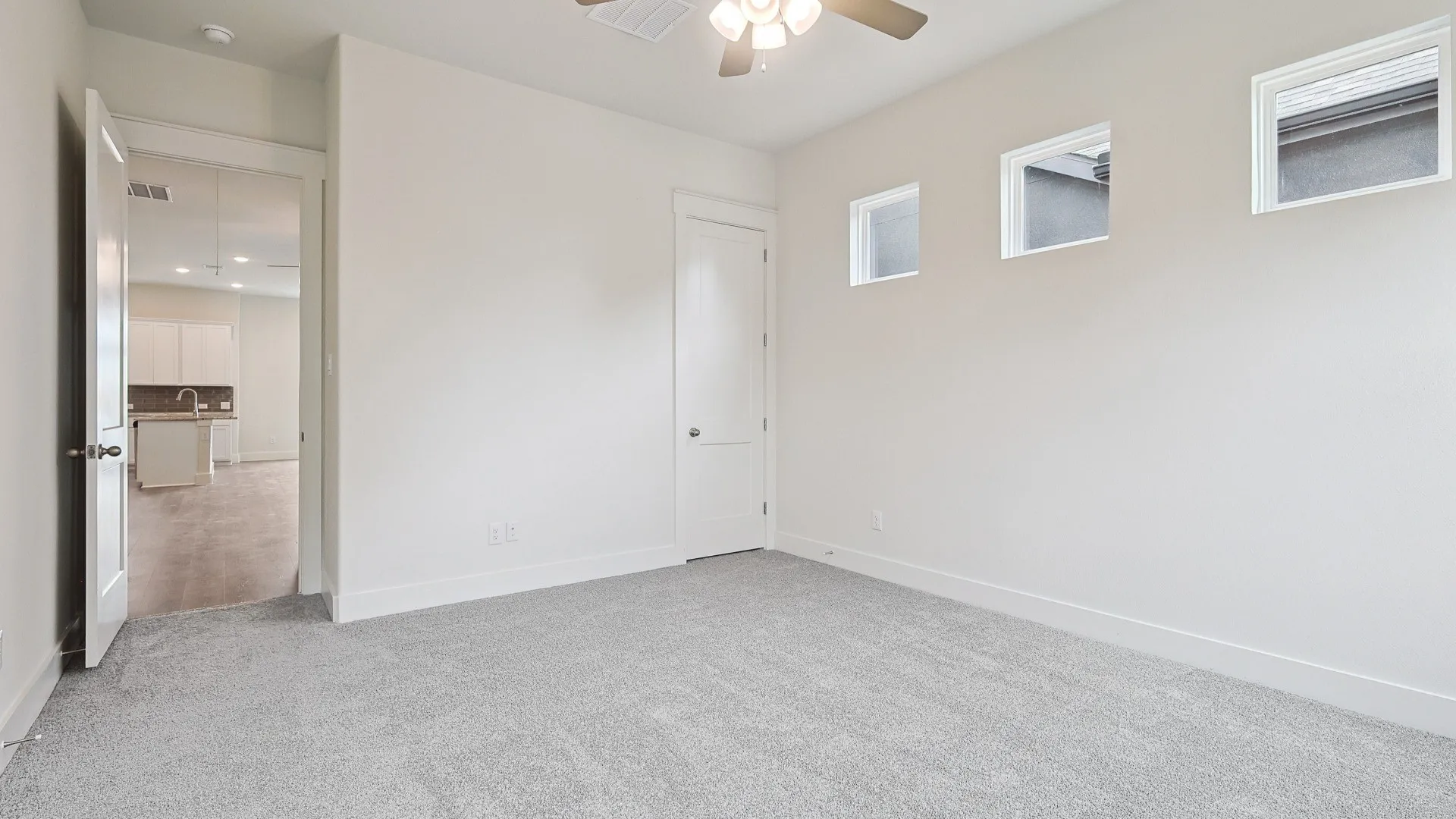 Carpeted room with ceiling fan, white walls, and three upper windows