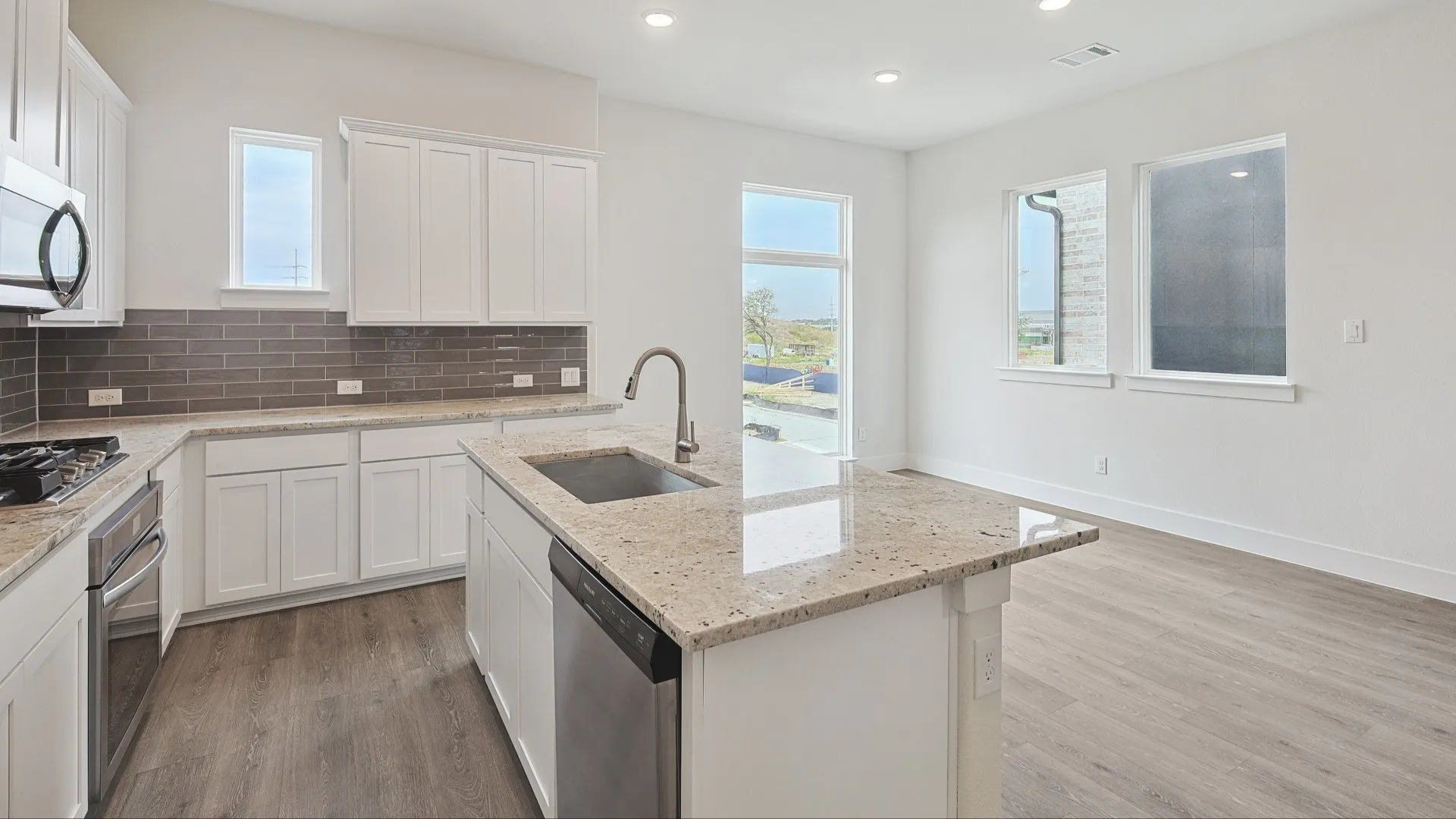 Modern kitchen featuring an island with an undermount sink, granite countertops, stainless steel appliances, white cabinetry, and wood-finish flooring