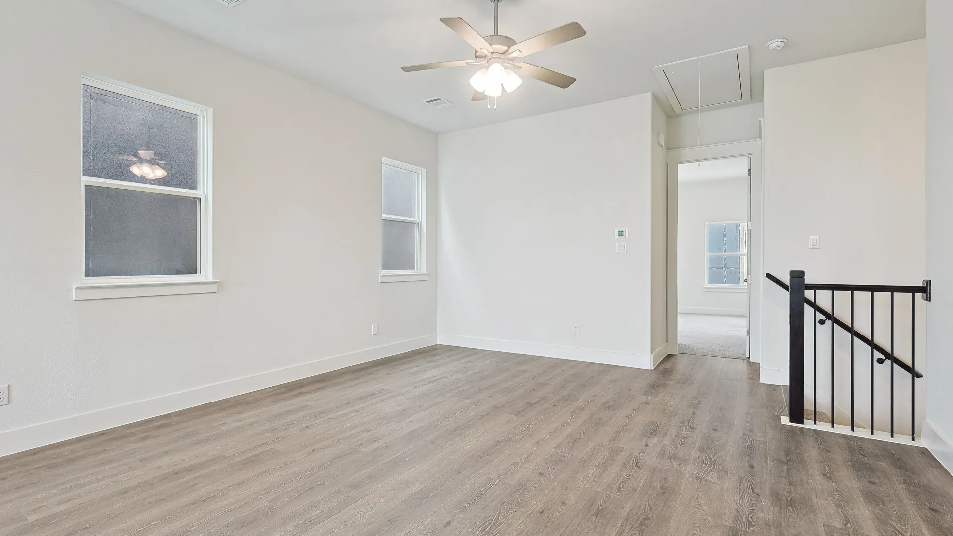 Spacious room with wood-finish flooring, two windows, and a ceiling fan