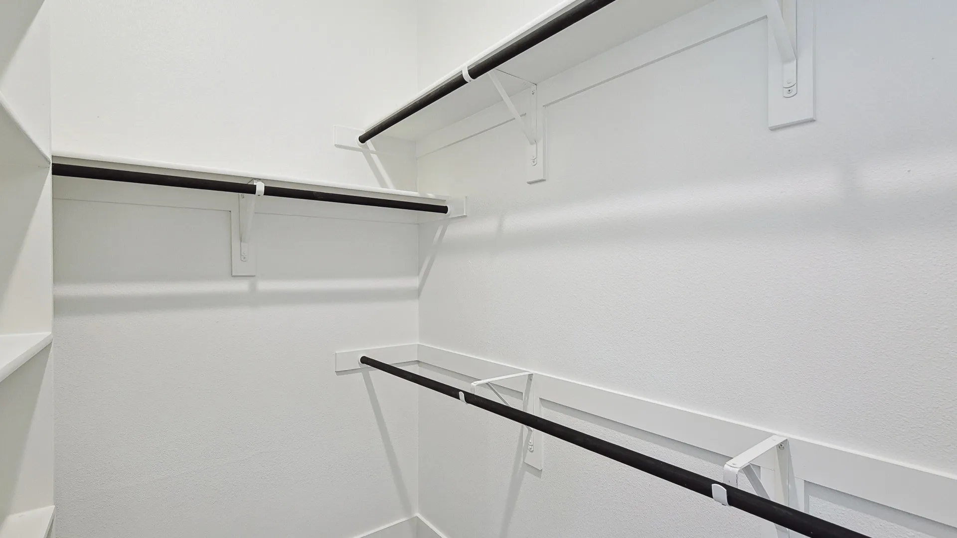 Walk-in closet featuring white walls, integrated shelving, and multiple hanging rods