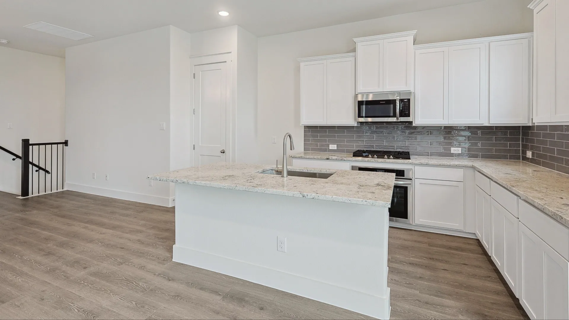 Contemporary kitchen featuring white cabinetry, light granite countertops, a subway tile backsplash, stainless steel appliances, and a central island with an integrated sink