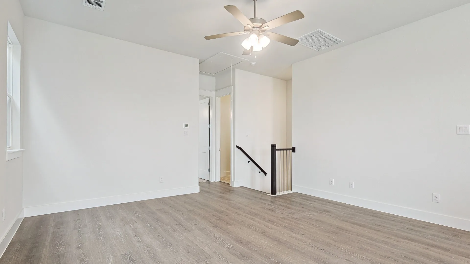 Spacious room featuring wood-finish flooring, a ceiling fan, and white baseboards