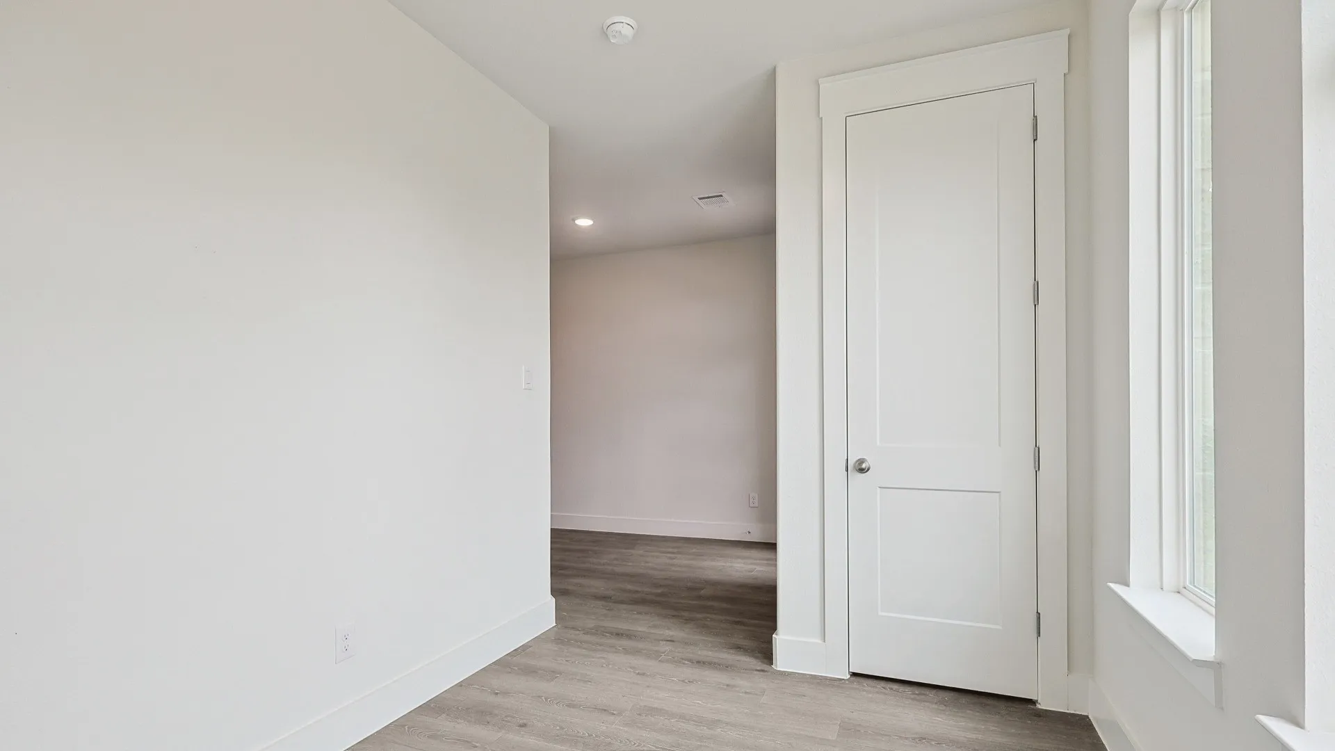 Light-filled interior space featuring wood-finish flooring, white trim, recessed lighting, and a two-panel door