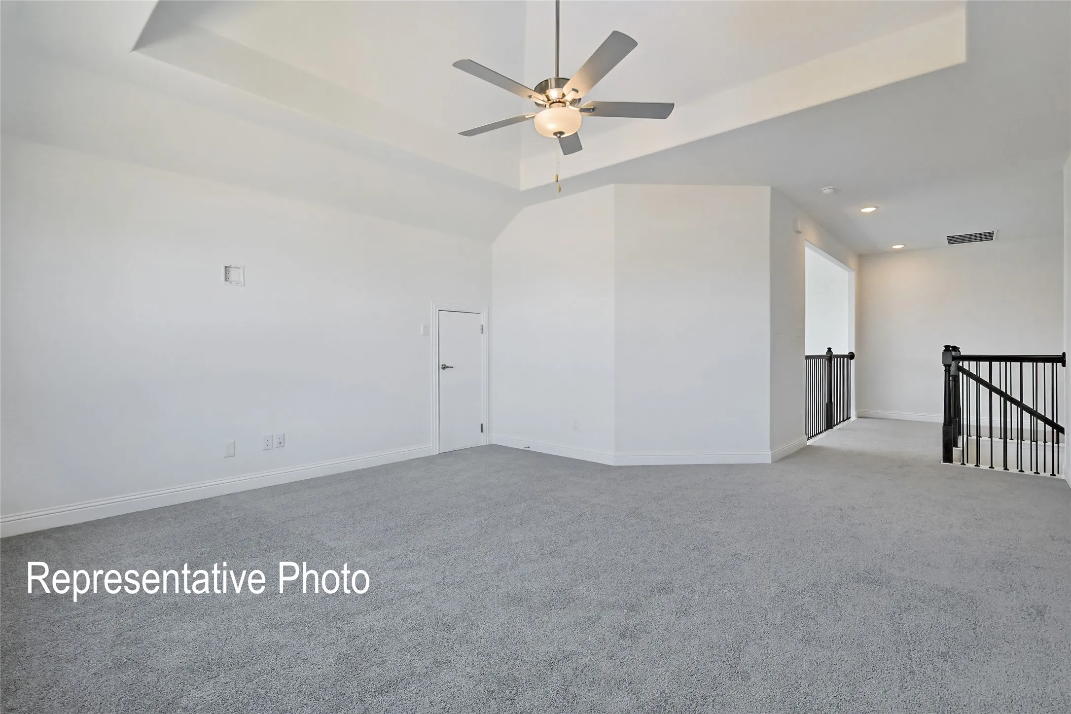 Spacious room featuring light gray carpeting, a tray ceiling, and a ceiling fan with integrated lighting