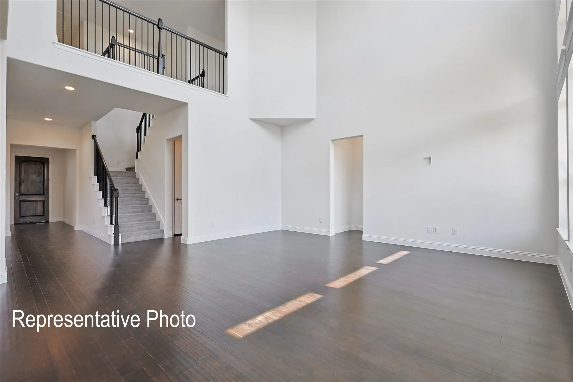 Vaulted living space featuring wood-finish flooring, a grand staircase with dark metal railings, an upper-level balcony, recessed lighting, and expansive windows
