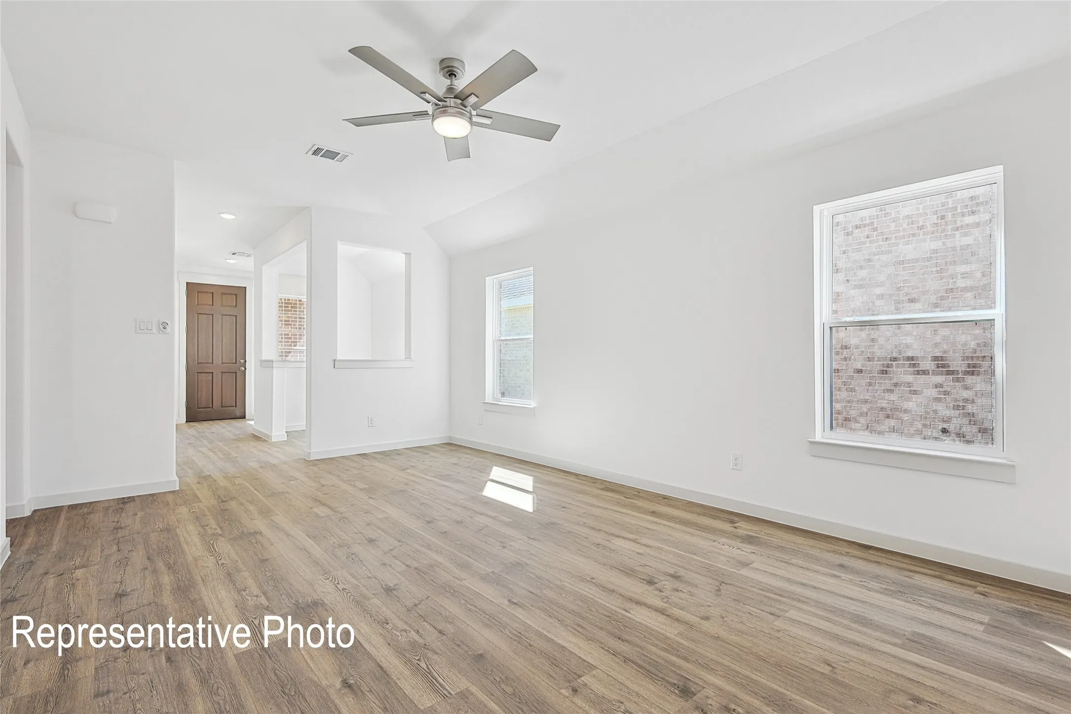 Spacious living area featuring wood-finish flooring, a contemporary ceiling fan with integrated lighting, and multiple windows