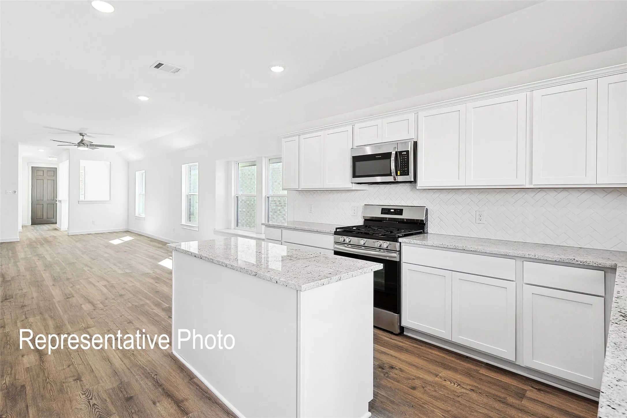 Modern kitchen featuring white cabinetry, granite countertops, a herringbone tile backsplash, stainless steel appliances, and a central island