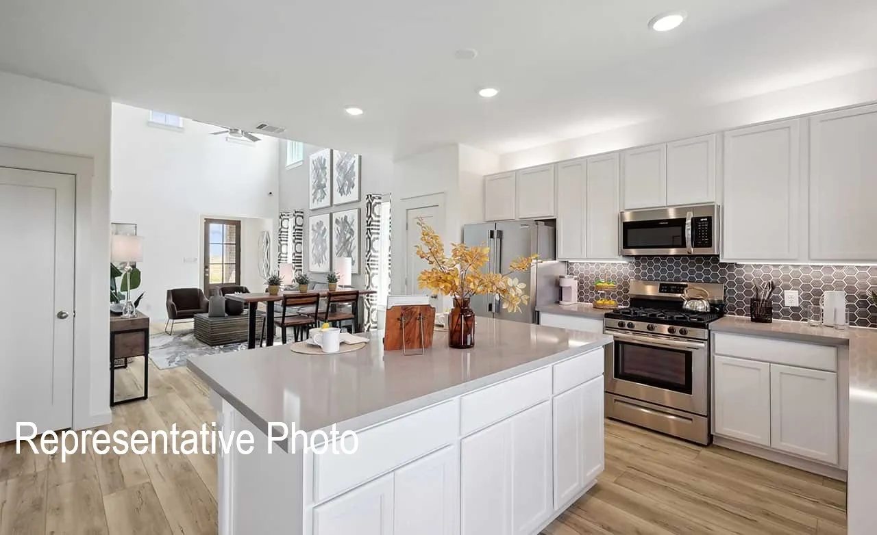 Open-concept kitchen featuring an island with a light-toned countertop, white cabinetry, stainless steel appliances, and a hexagonal tile backsplash