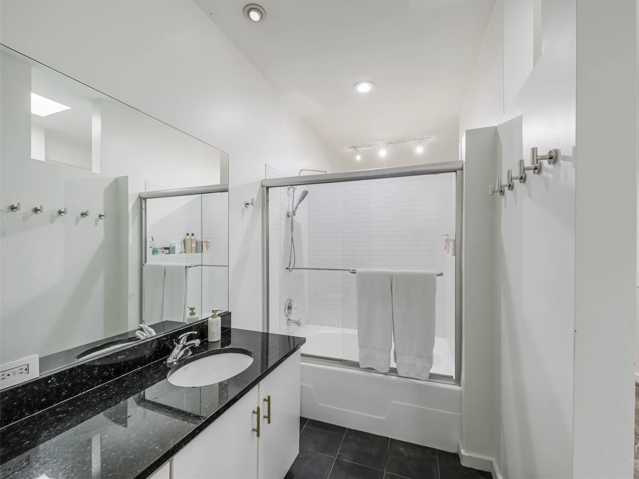Primary Bathroom featuring a vanity with a black countertop and an undermount sink, a large wall mirror, and a tub-shower combination with a sliding glass enclosure