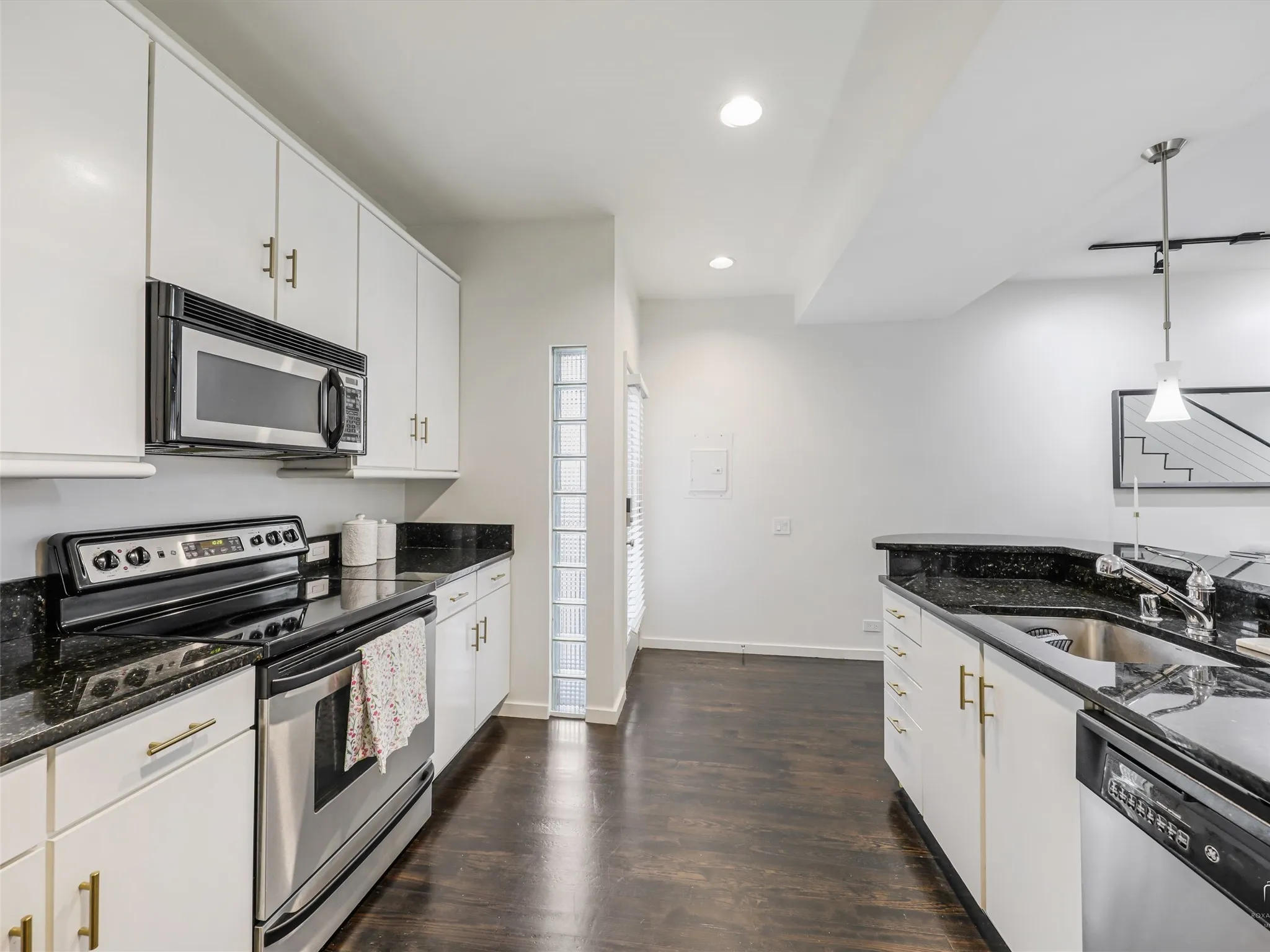 Kitchen featuring dark wood-finish flooring, white cabinetry with gold-tone hardware, and dark countertops
