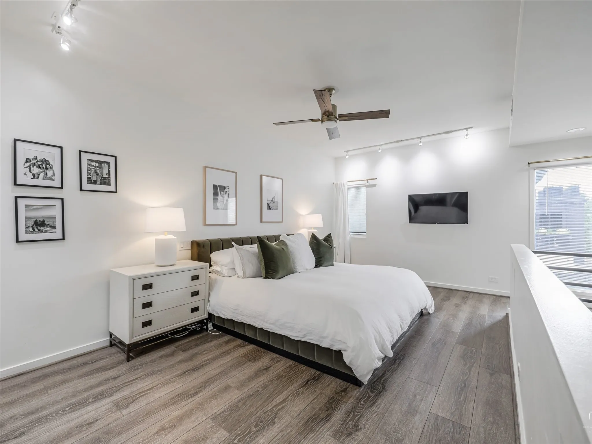 Spacious room featuring wood-finish flooring, high ceilings, ceiling fan, track lighting, and abundant natural light from multiple windows