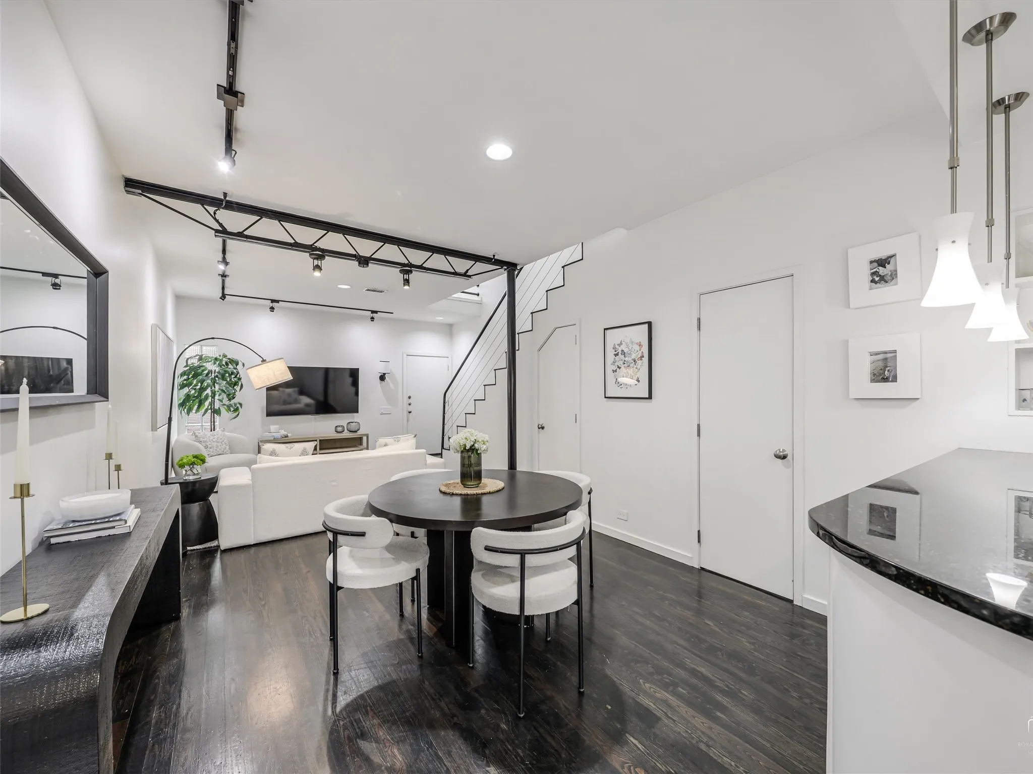 Open-concept living space featuring rich wood-finish flooring, a contemporary floating staircase with metal railings, and modern track lighting