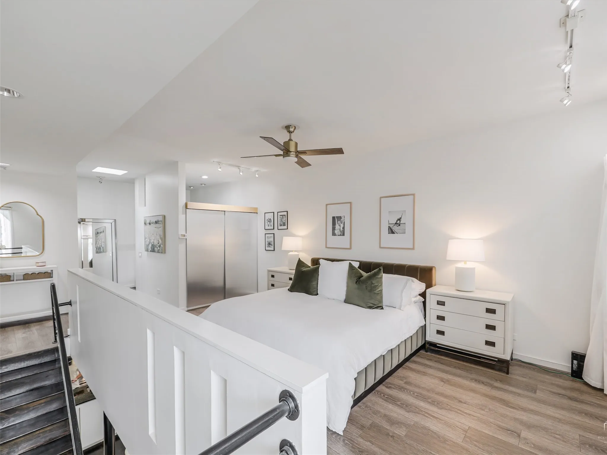 Loft-style room featuring wood-finish flooring, a contemporary ceiling fan, track lighting, and a white panel railing